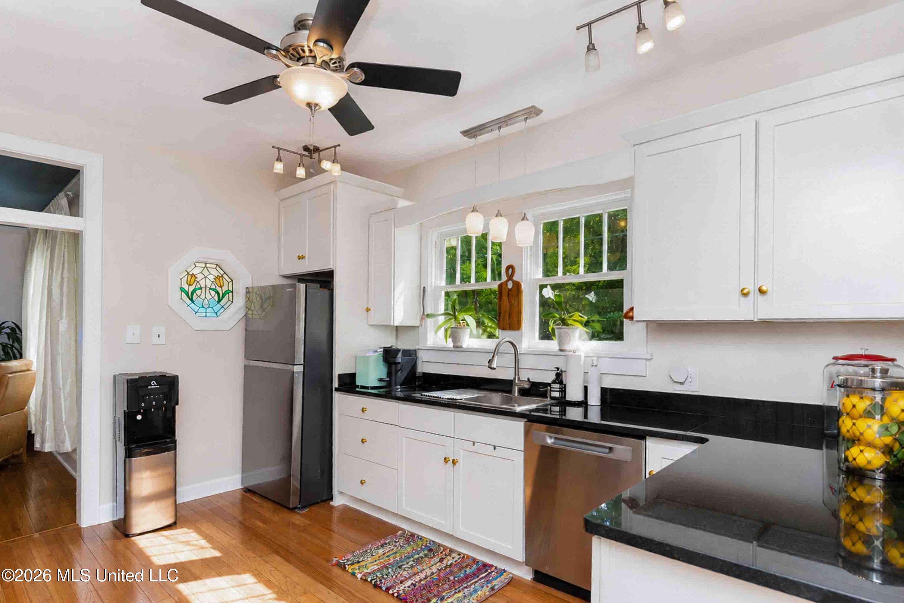 Bright kitchen with white cabinets, black countertops, stainless steel appliances, and a sink beneath sunny windows.