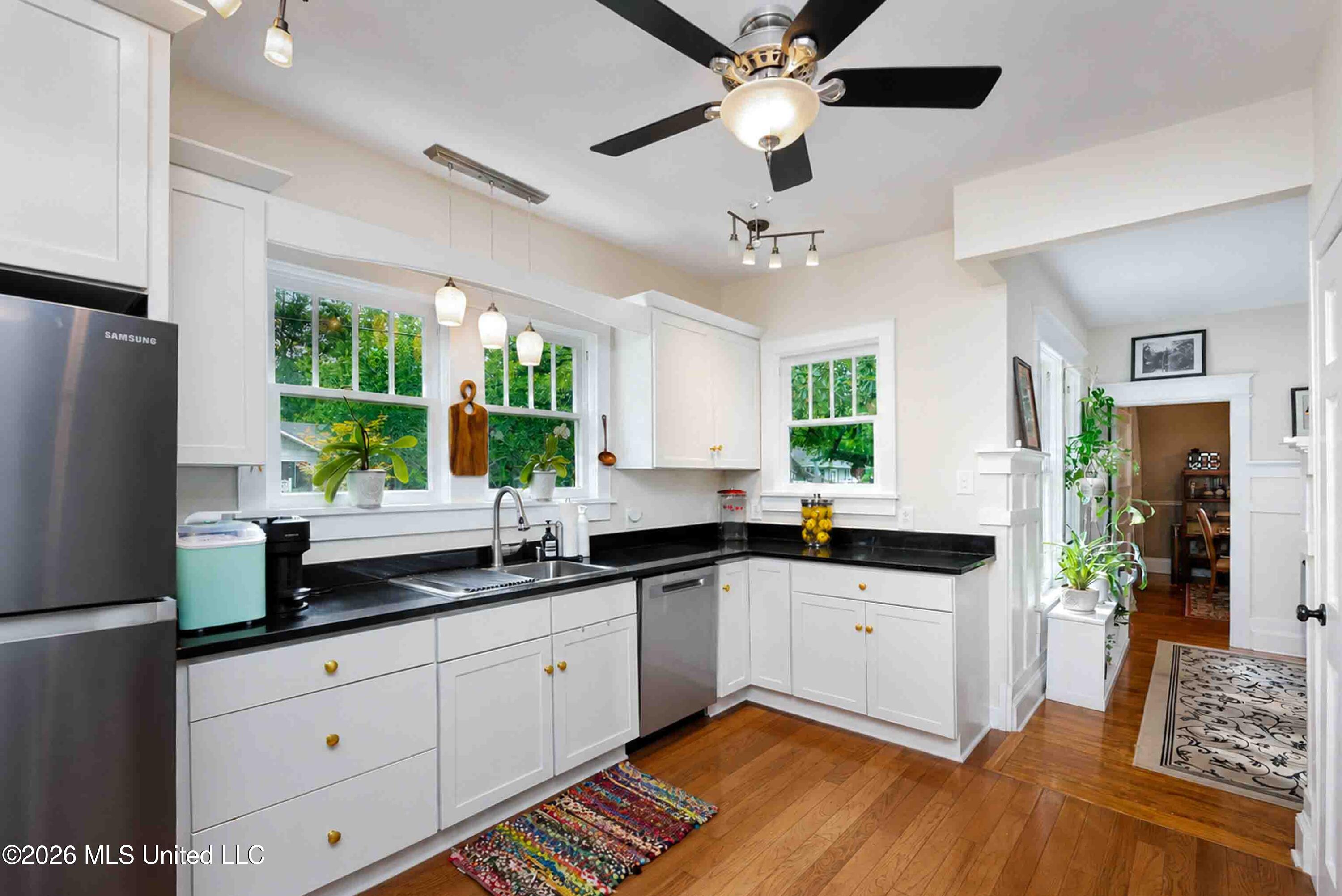 Bright kitchen with white cabinets, black countertops, stainless appliances, and windows overlooking greenery.