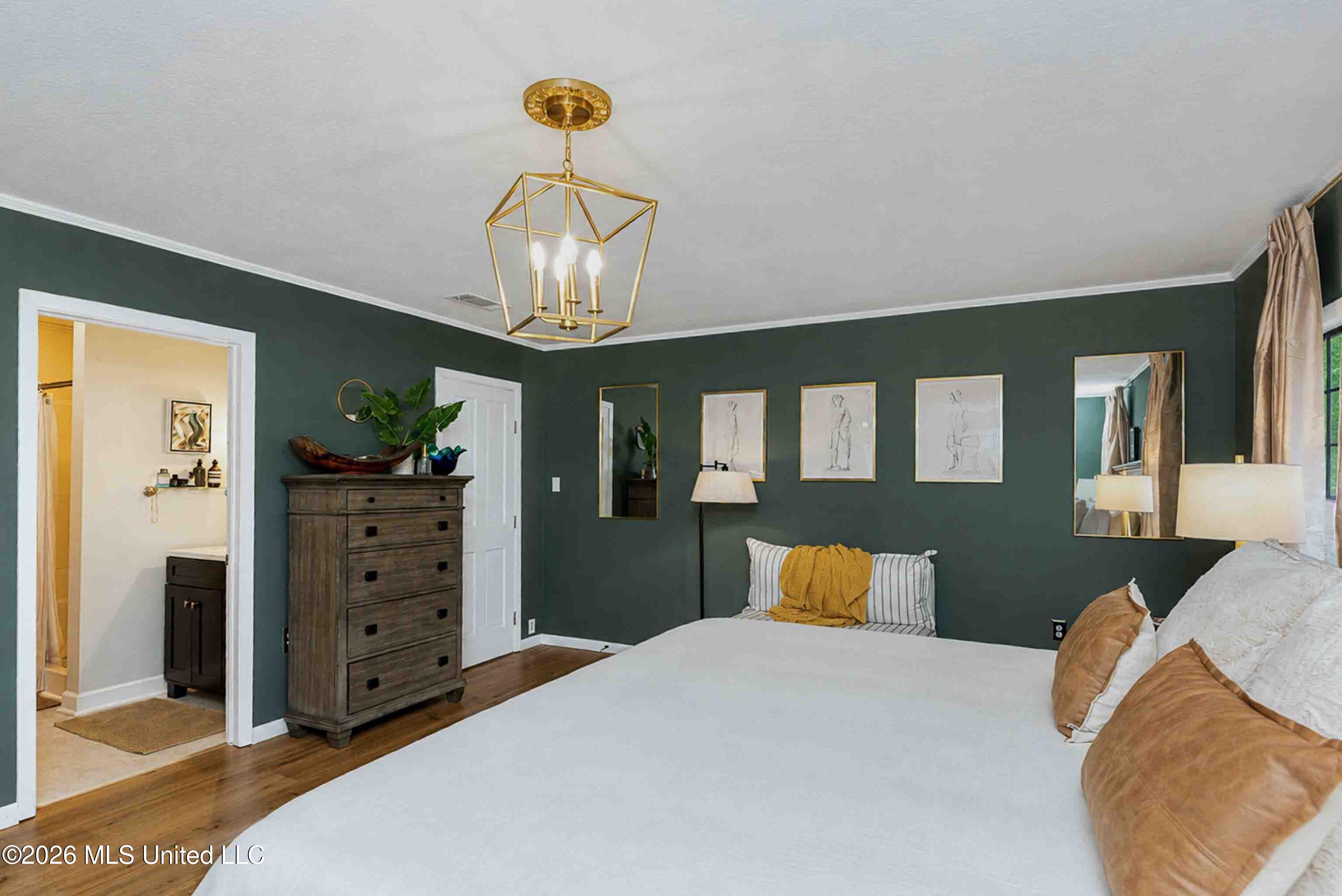 Furnished bedroom with dark green walls, a white bed, wooden chest of drawers, and gold pendant light.