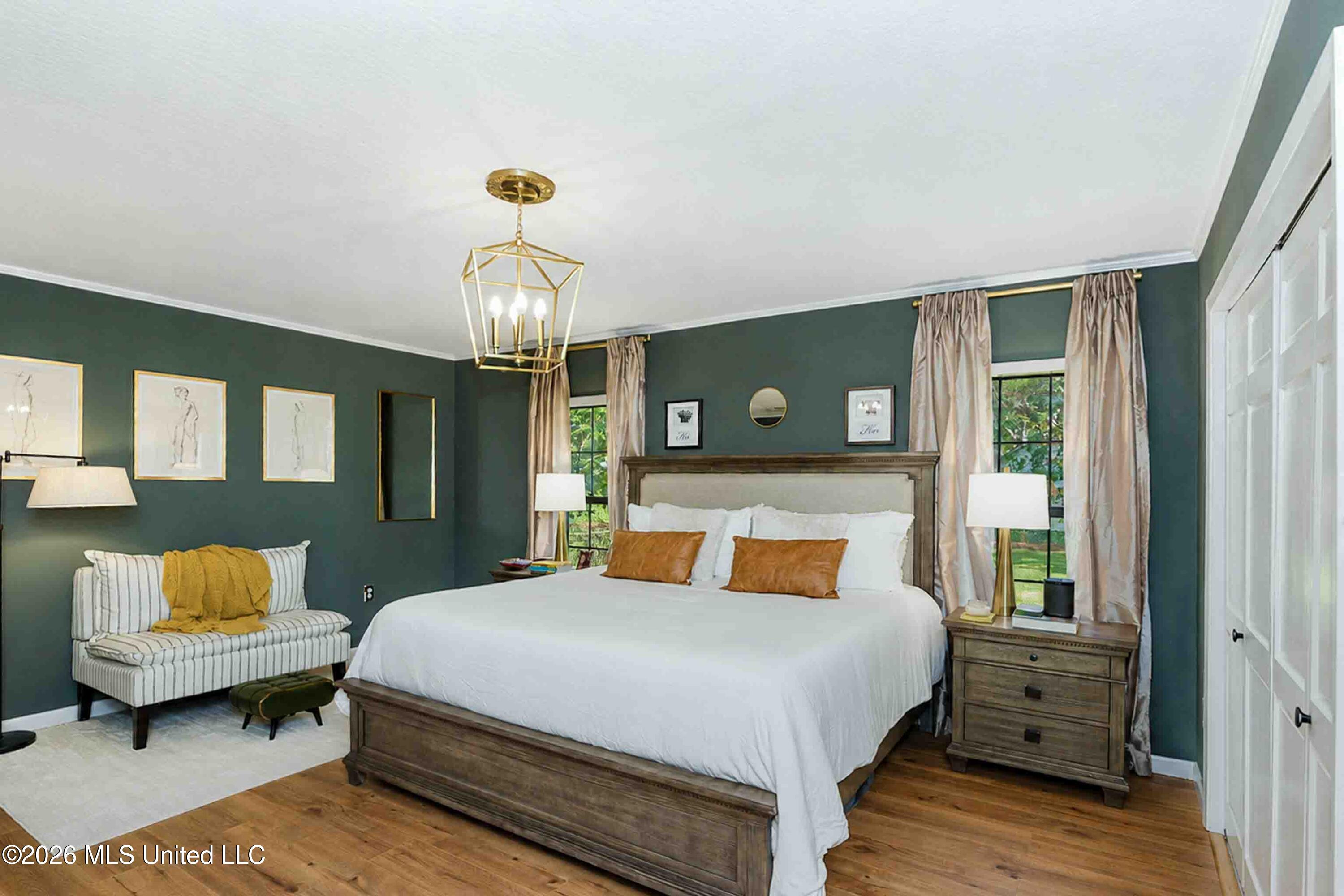 Bedroom with dark green walls, a large white bed, striped settee, and brass chandelier.