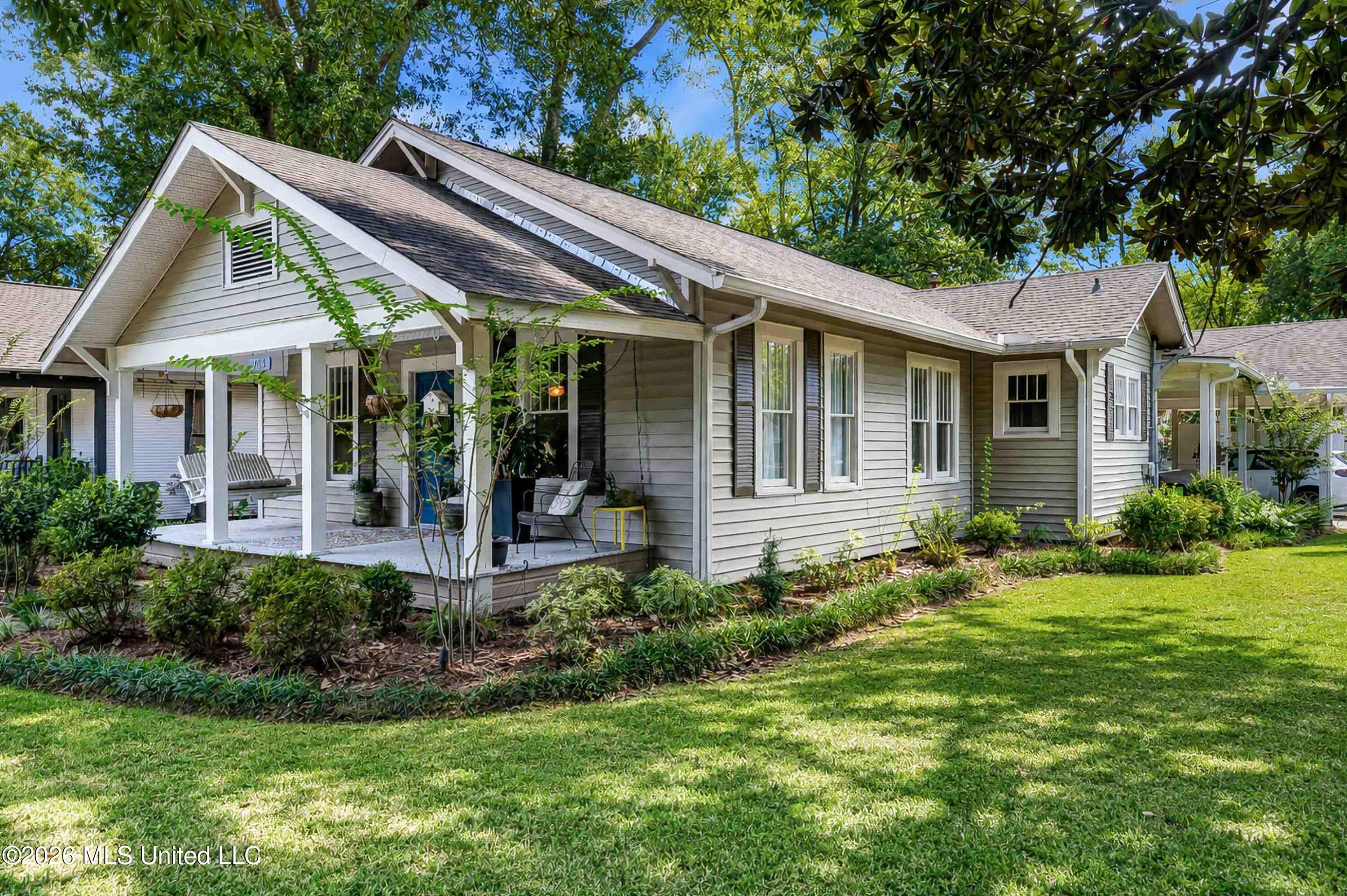 Gray-sided house with a covered front porch, white trim, and mature trees in the yard.