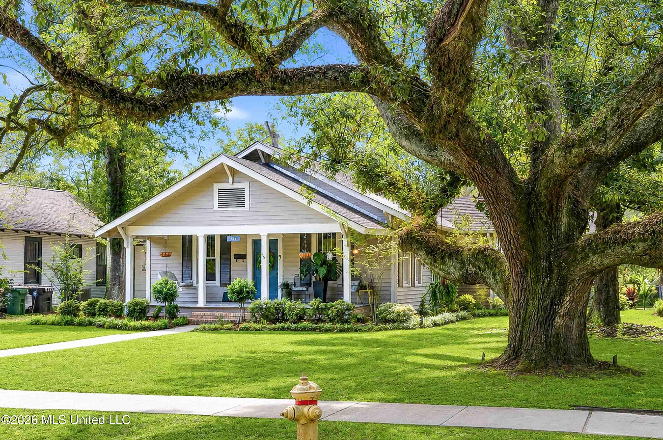 Home with a covered porch and blue door beneath a large oak tree.