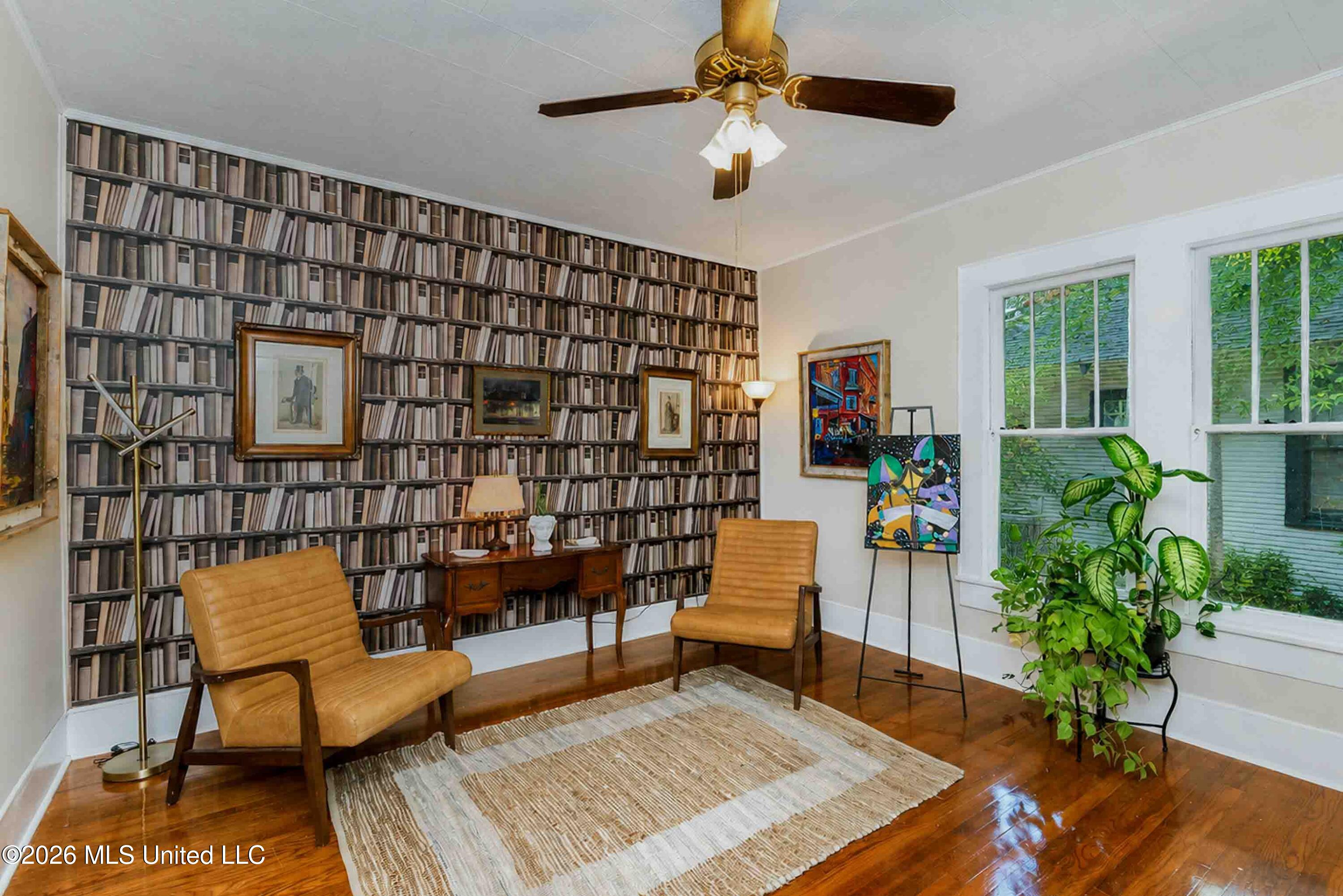 Study with bookcase-patterned wallpaper, tan leather chairs, and tall windows.
