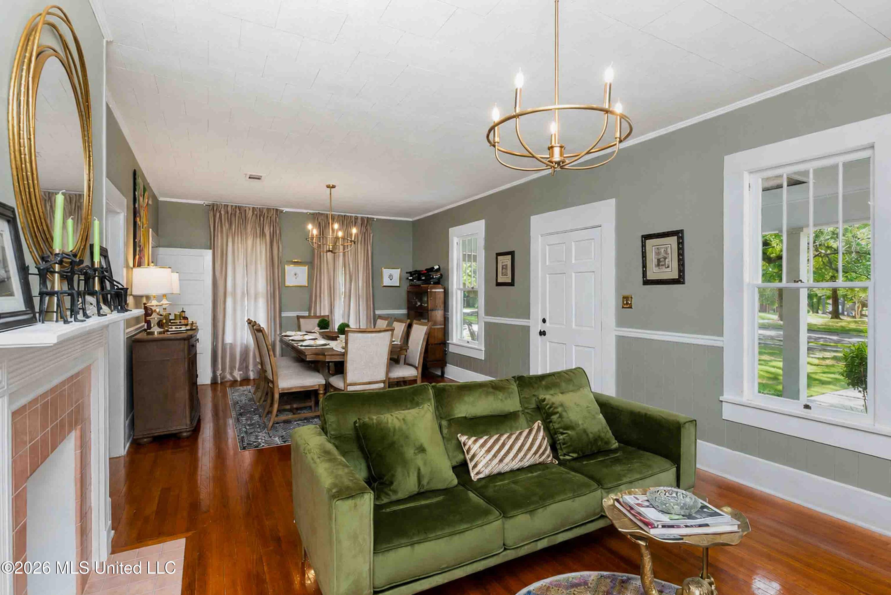 Living and dining room with a green sofa, brick fireplace, and polished hardwood floors.