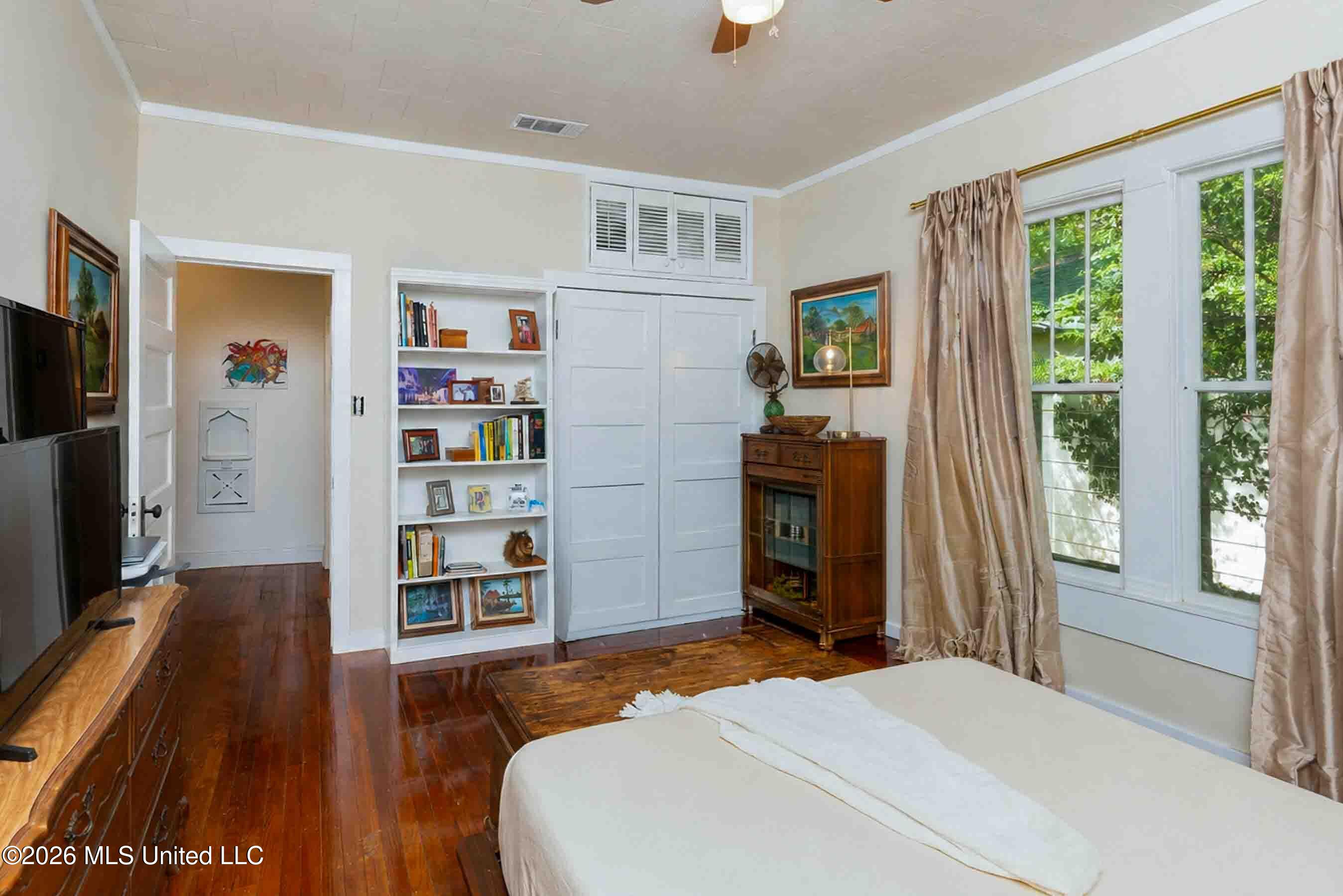 Bedroom with built-in bookshelves and closets, hardwood floors, and tall curtained windows.