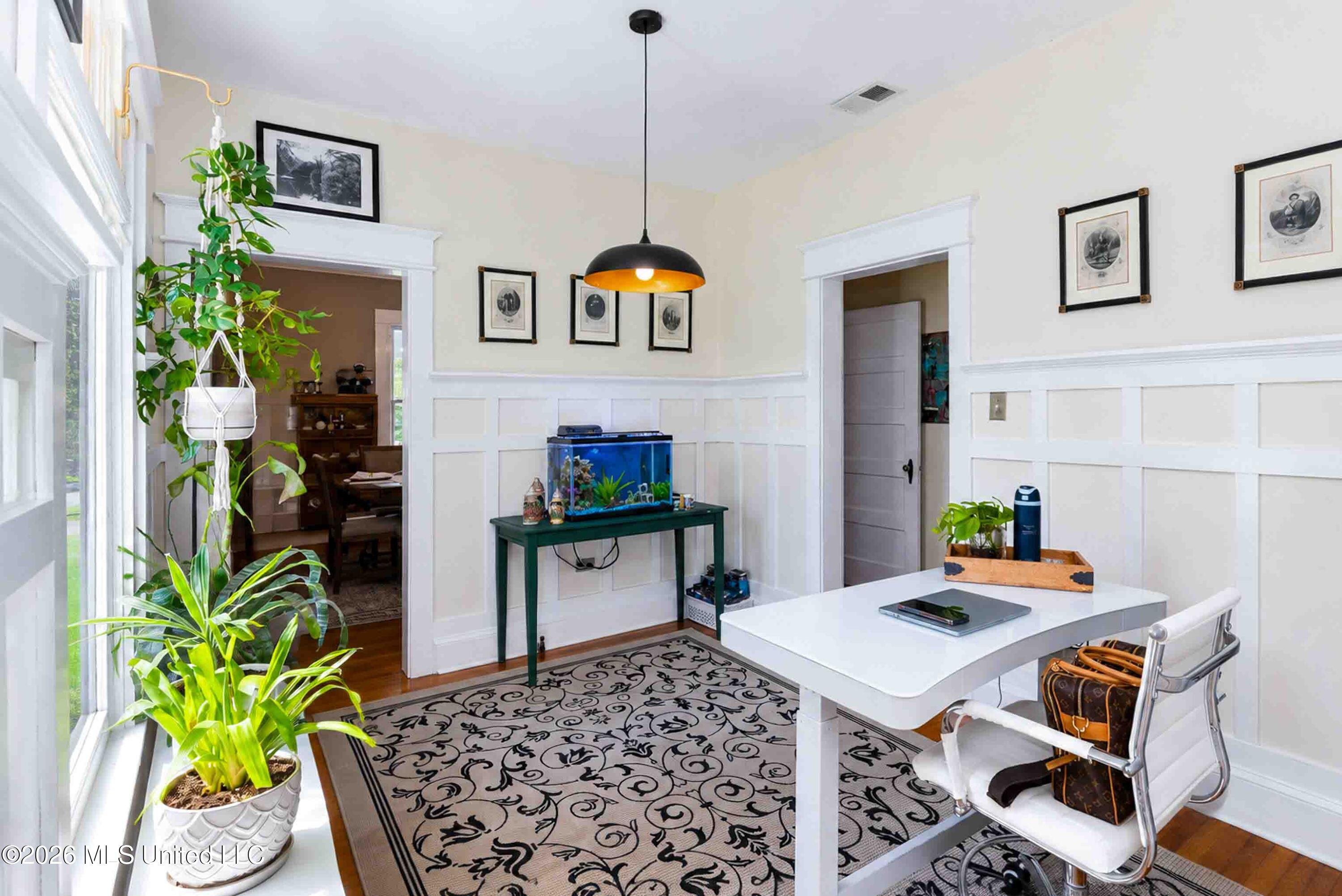 Furnished room with white paneled walls, a patterned rug, plants, and a fish tank.