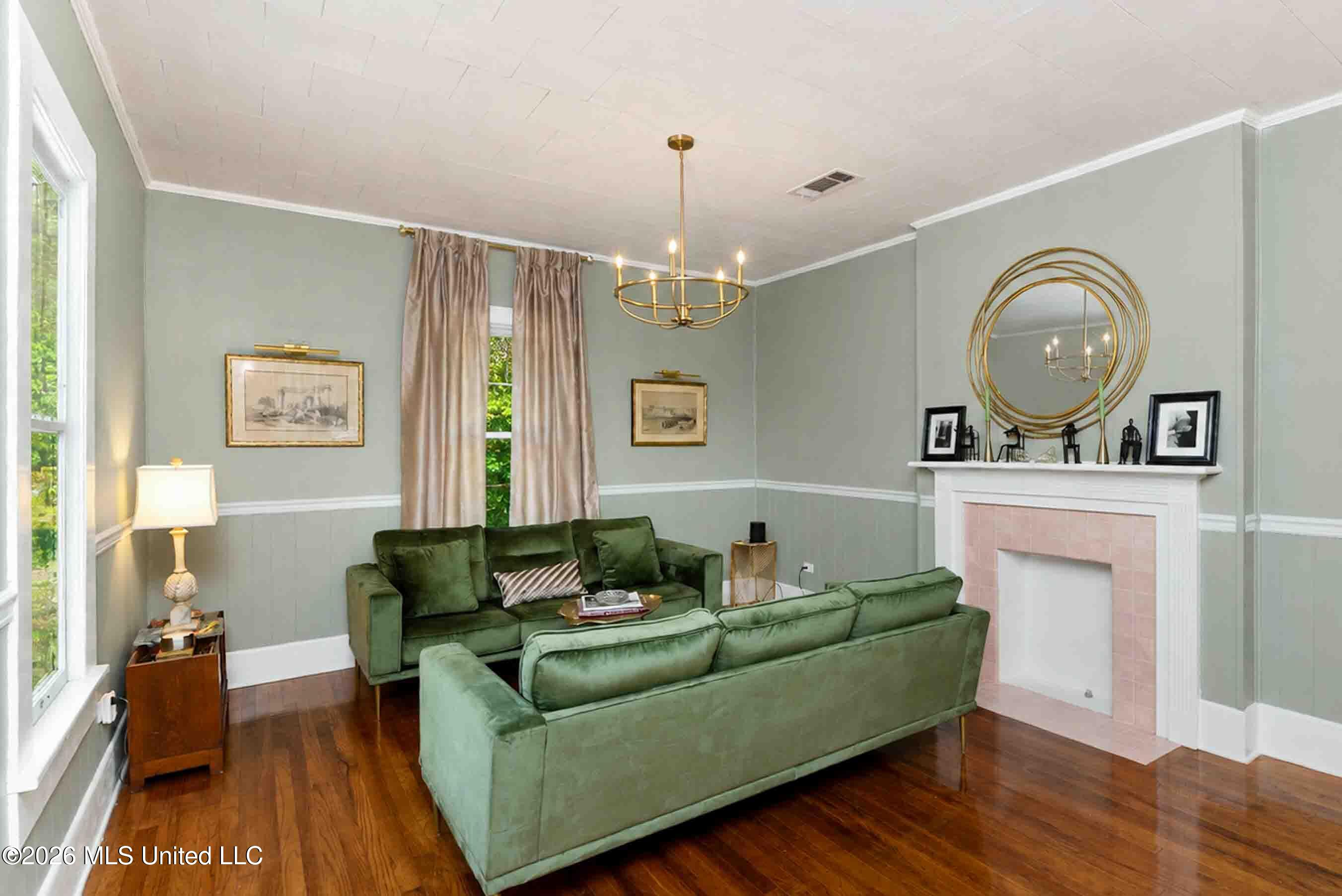 Living room with green sofas, hardwood floors, and a white fireplace with pink tile surround.