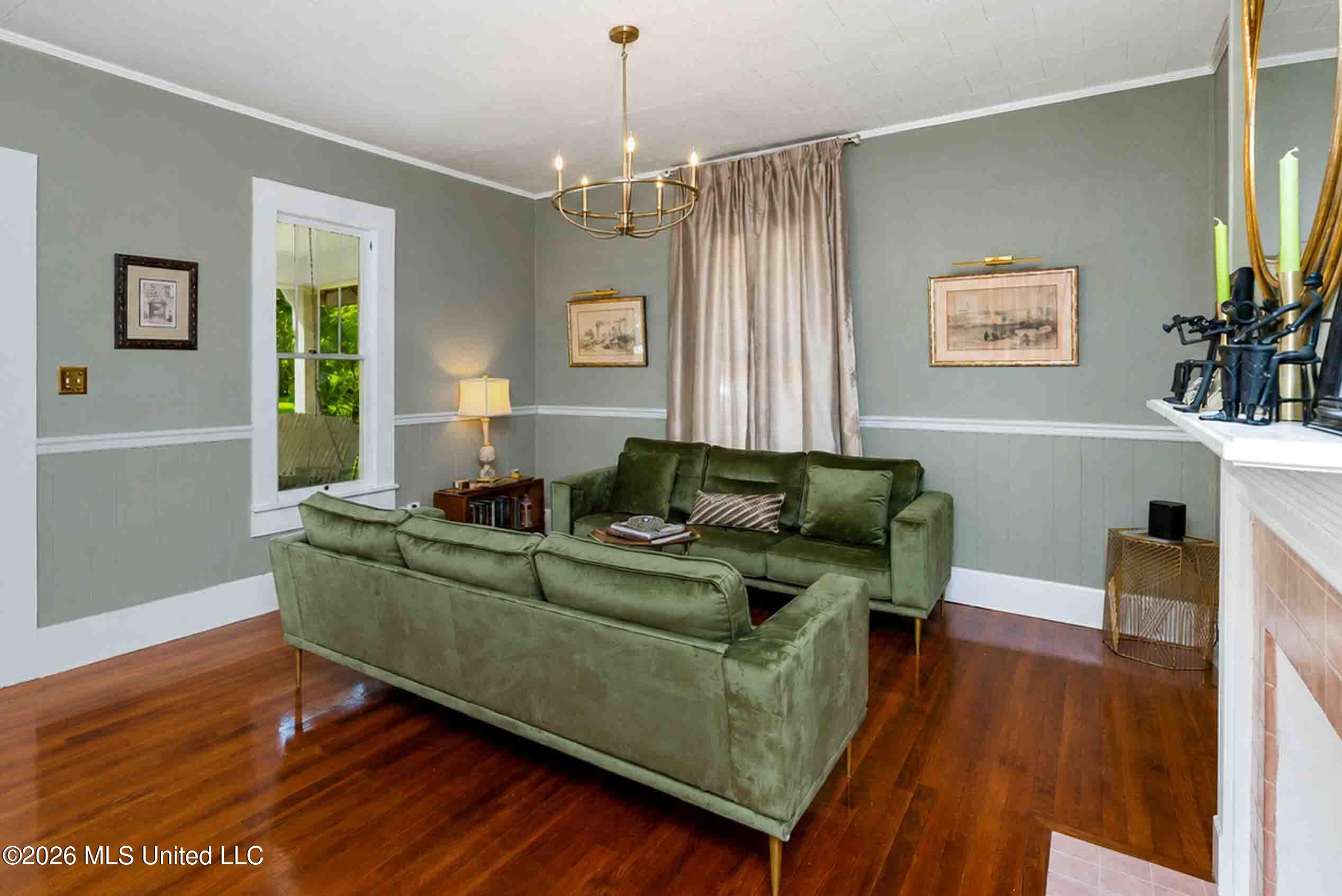 Living room with green sofas, polished hardwood floors, and a brass chandelier.