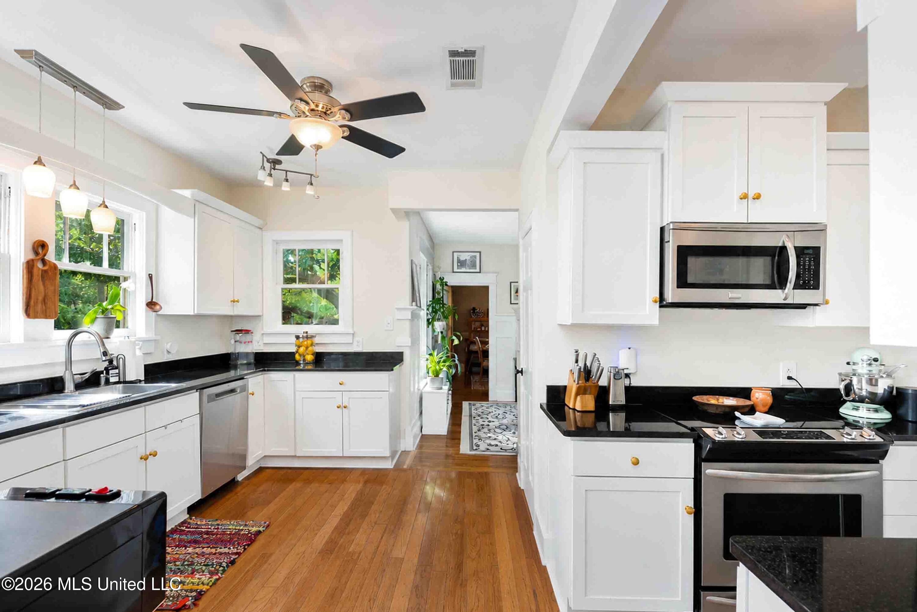 Bright kitchen with white cabinets, black countertops, stainless steel appliances, and hardwood floors.