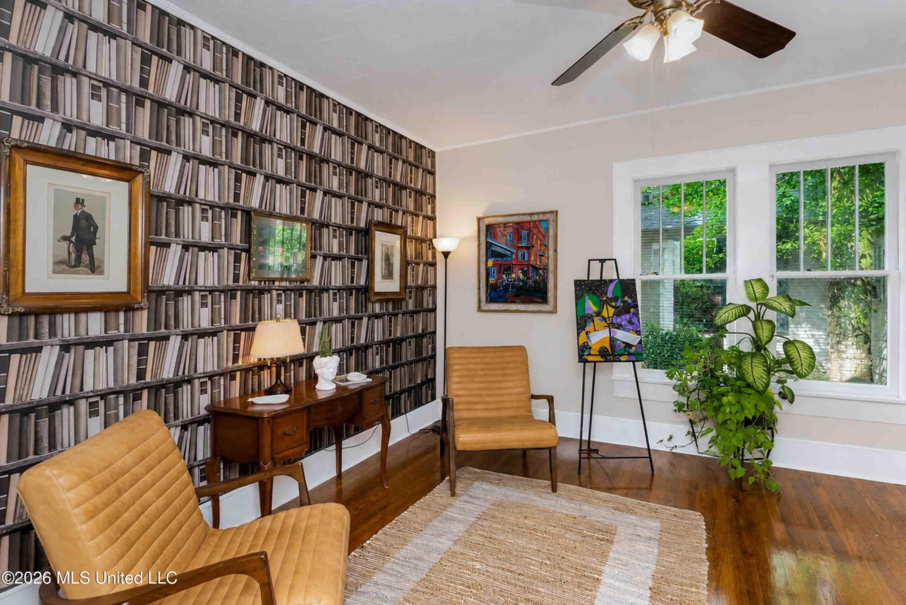 Study with bookshelf-patterned walls, tan leather chairs, a wooden desk, and windows overlooking greenery.