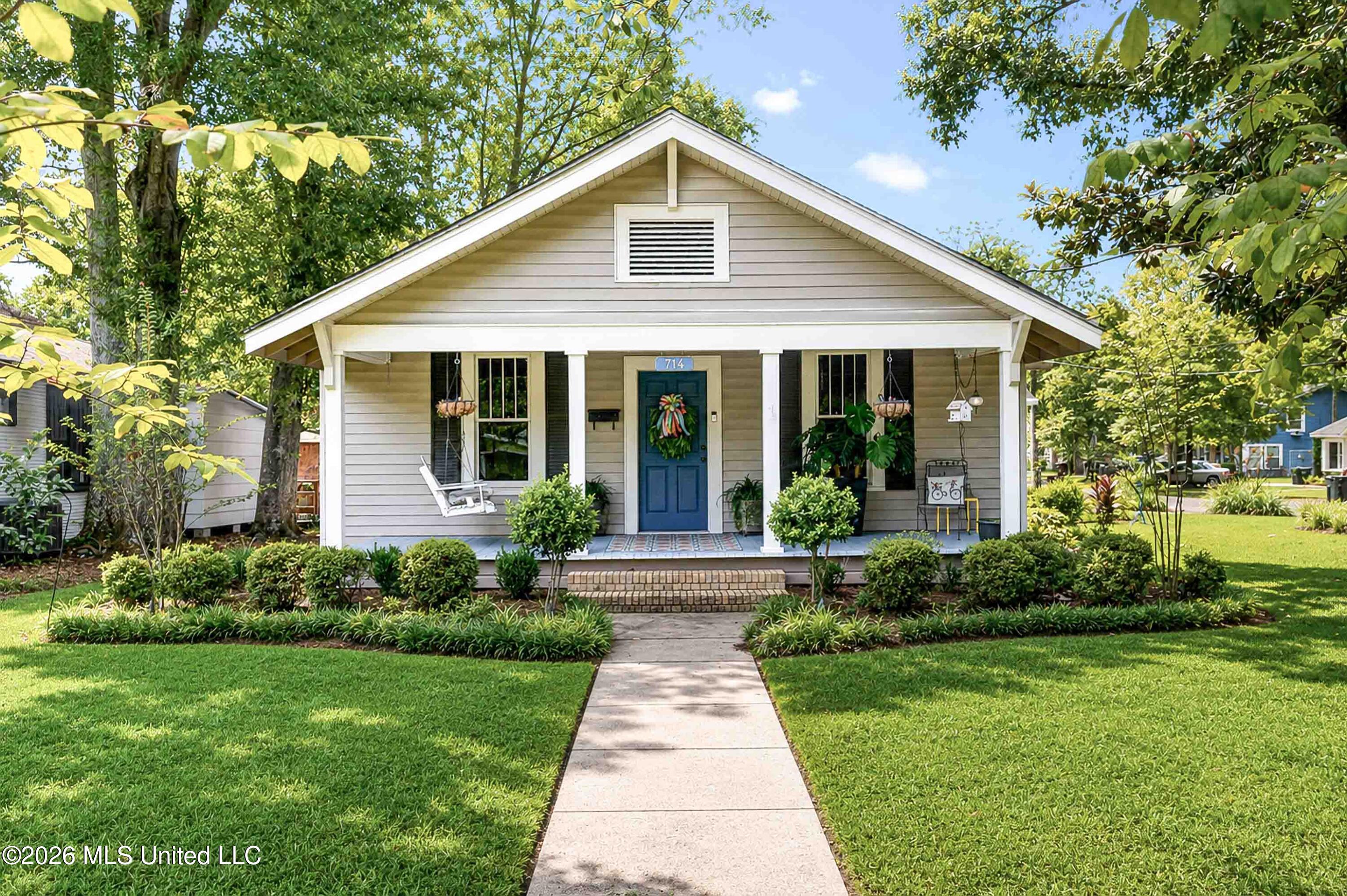 Front exterior of a gray cottage with a blue door, porch swing, and landscaped lawn.