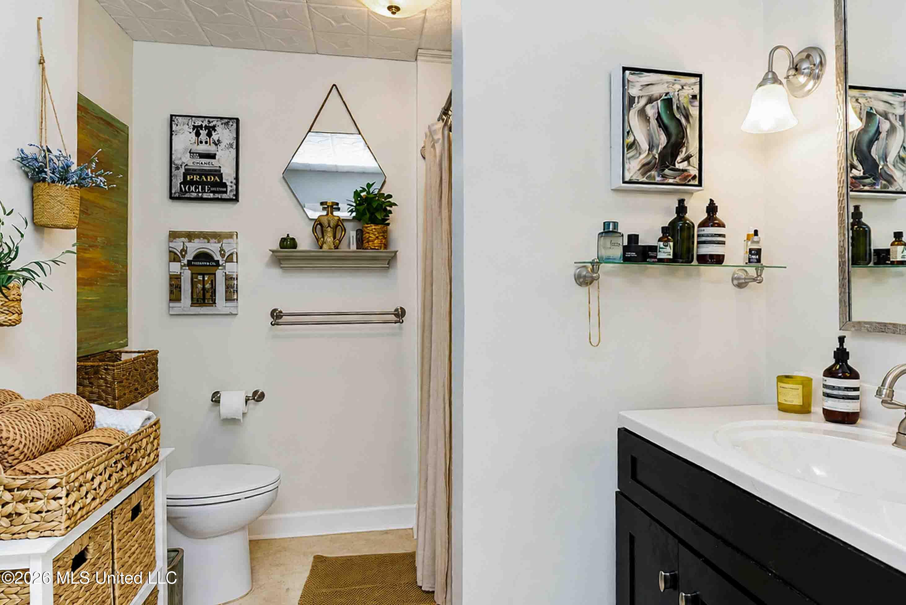 Bathroom with a dark vanity, white countertop, beige shower curtain, and woven storage baskets.