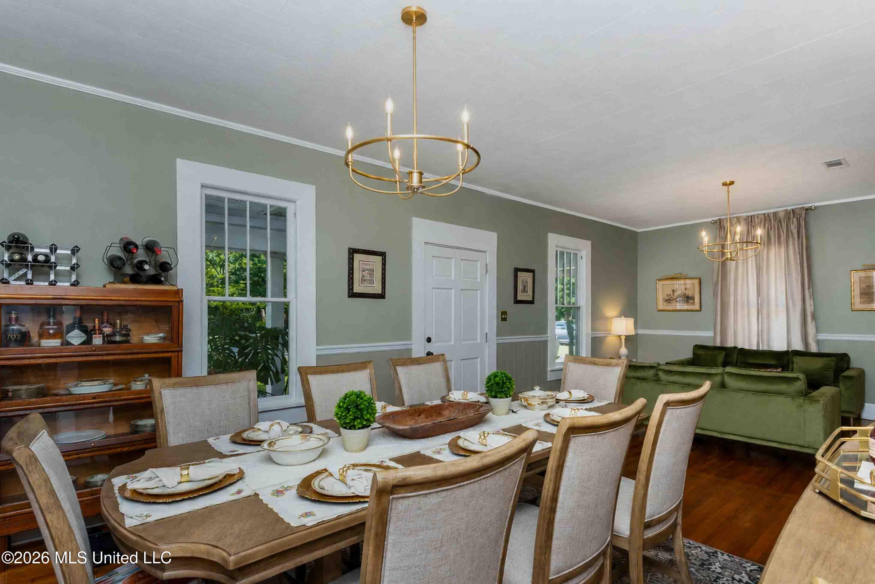 Dining room with a set table, wooden china cabinet, and adjoining living area with a green sofa.