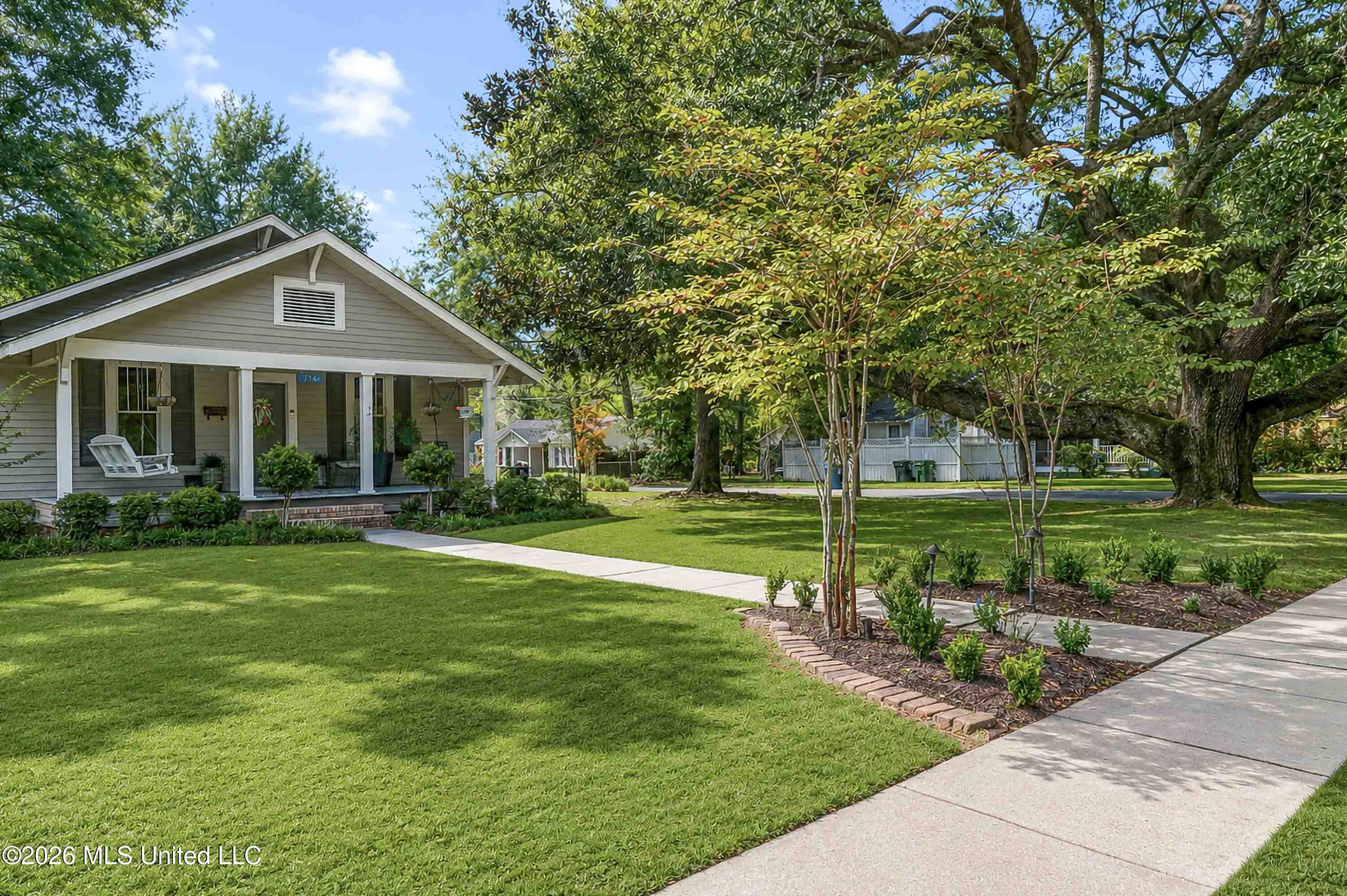 Gray house with a covered front porch, broad lawn, and mature shade trees.