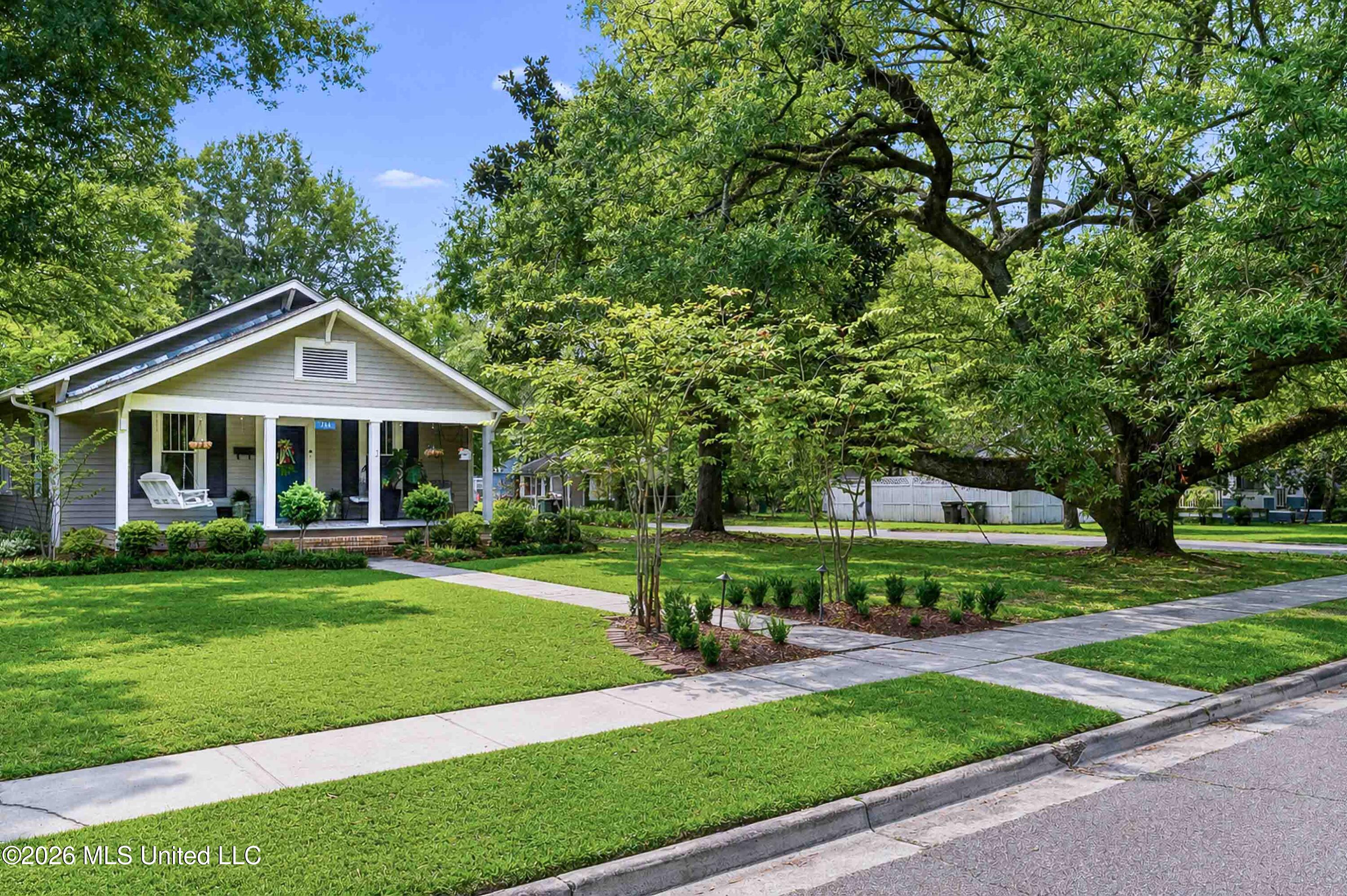 Gray cottage with a covered porch and blue door beneath large shade trees.