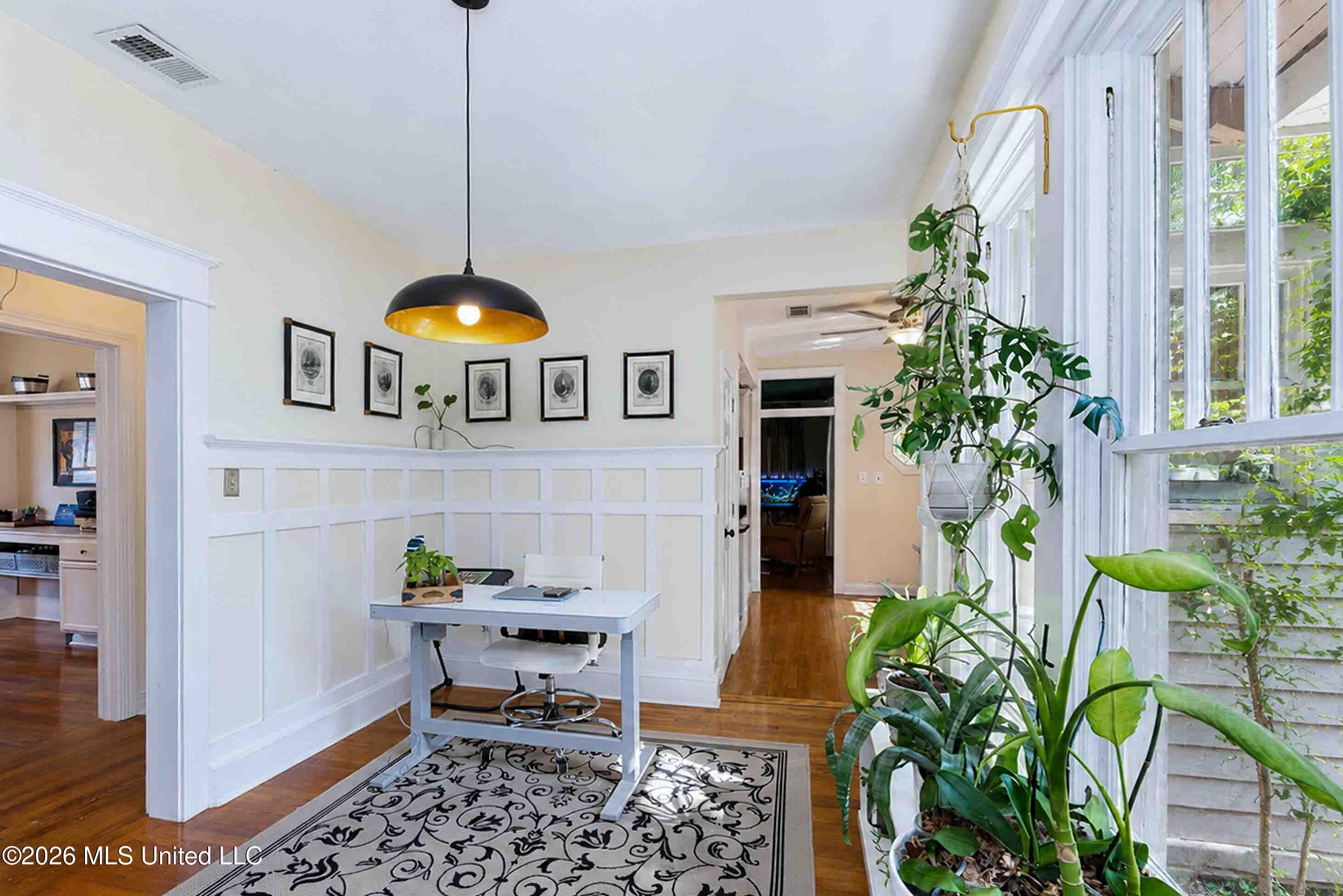 Bright home office nook with a white desk, paneled walls, and tall windows.