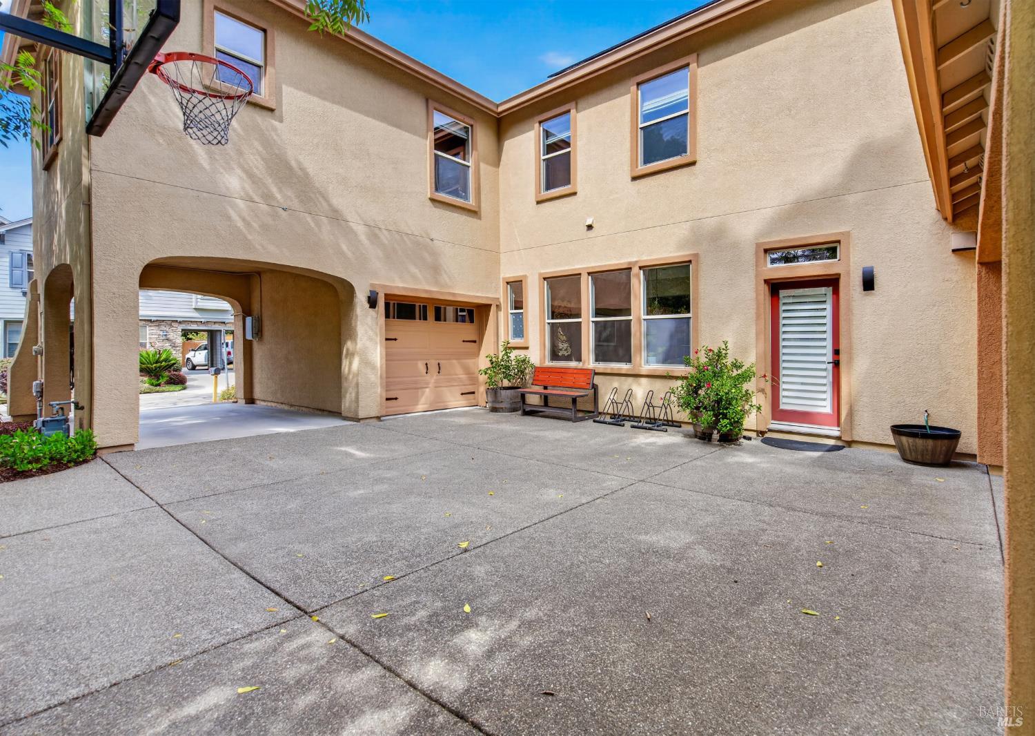 Two-story stucco home with a broad concrete courtyard, garage, covered passage, and basketball hoop.