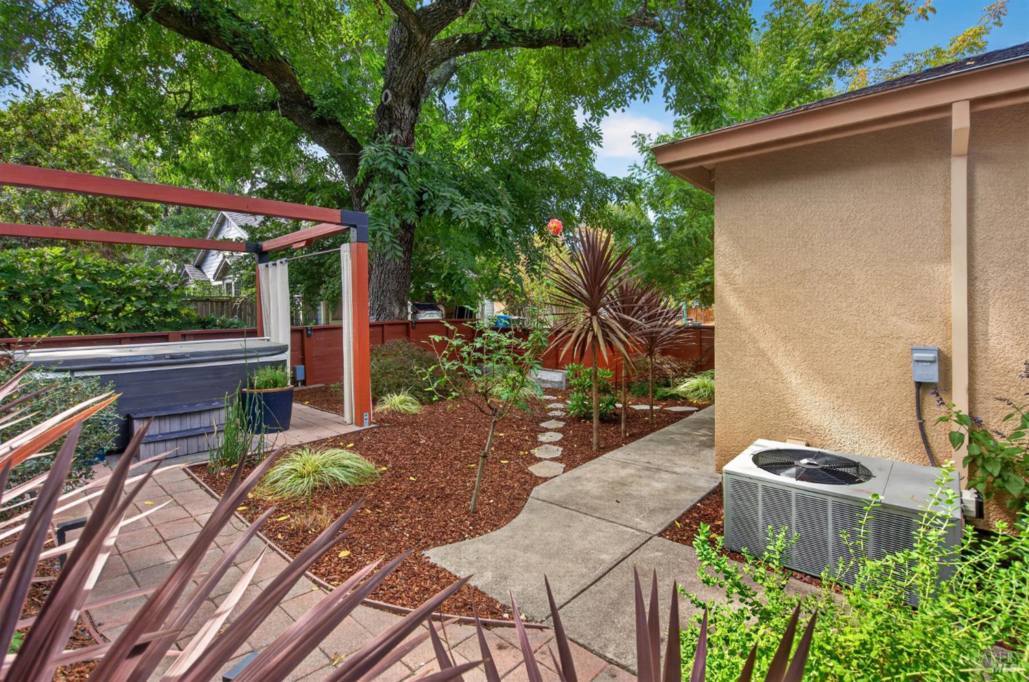 Landscaped backyard with a hot tub under a pergola and stepping stones through the garden.
