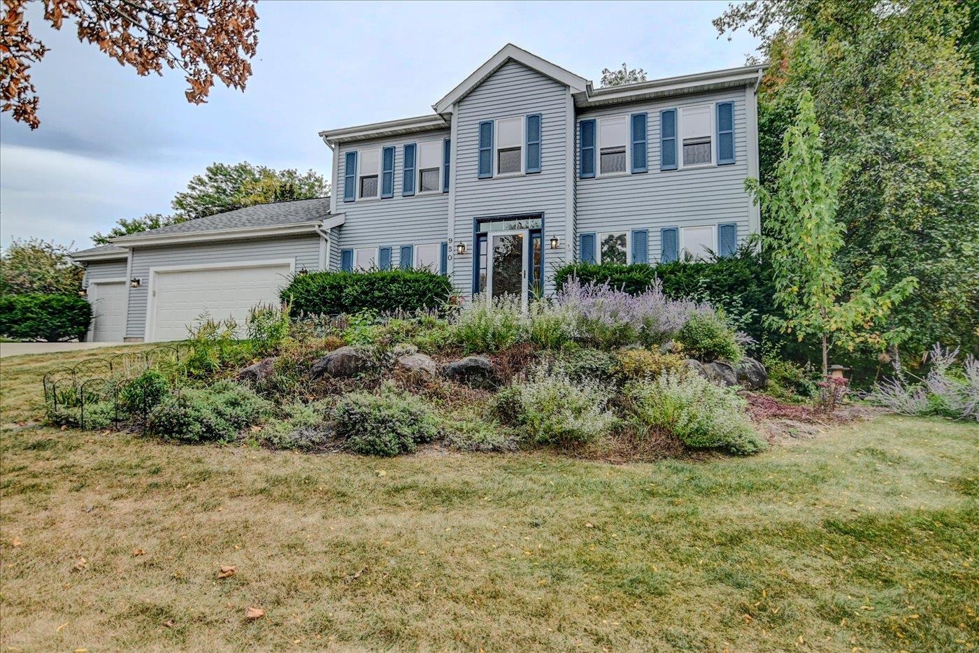 Two-story gray house with blue shutters, attached garage, and landscaped garden.