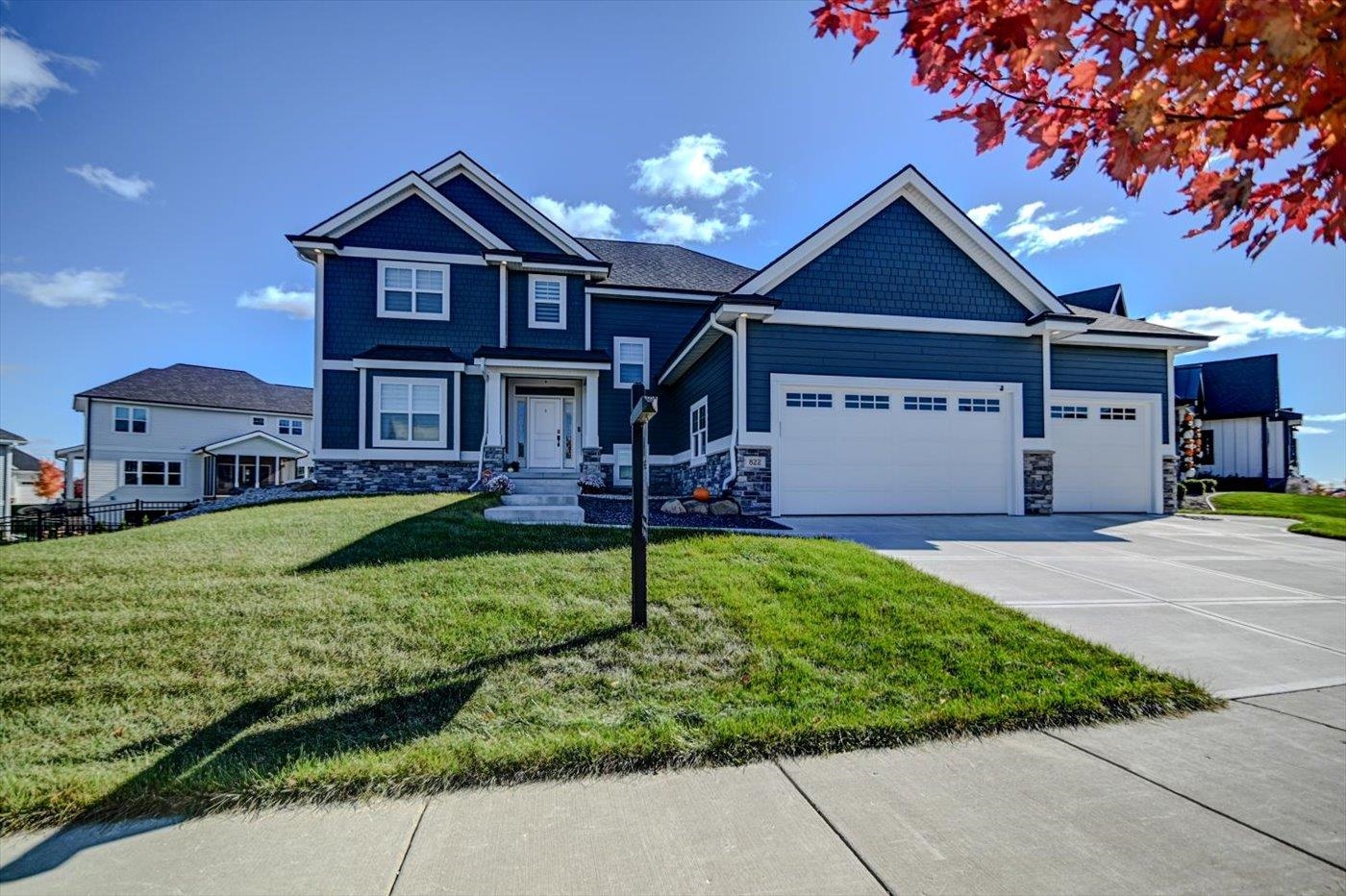 Two-story blue house with white trim, stone accents, and a three-car garage beside a sloping lawn.