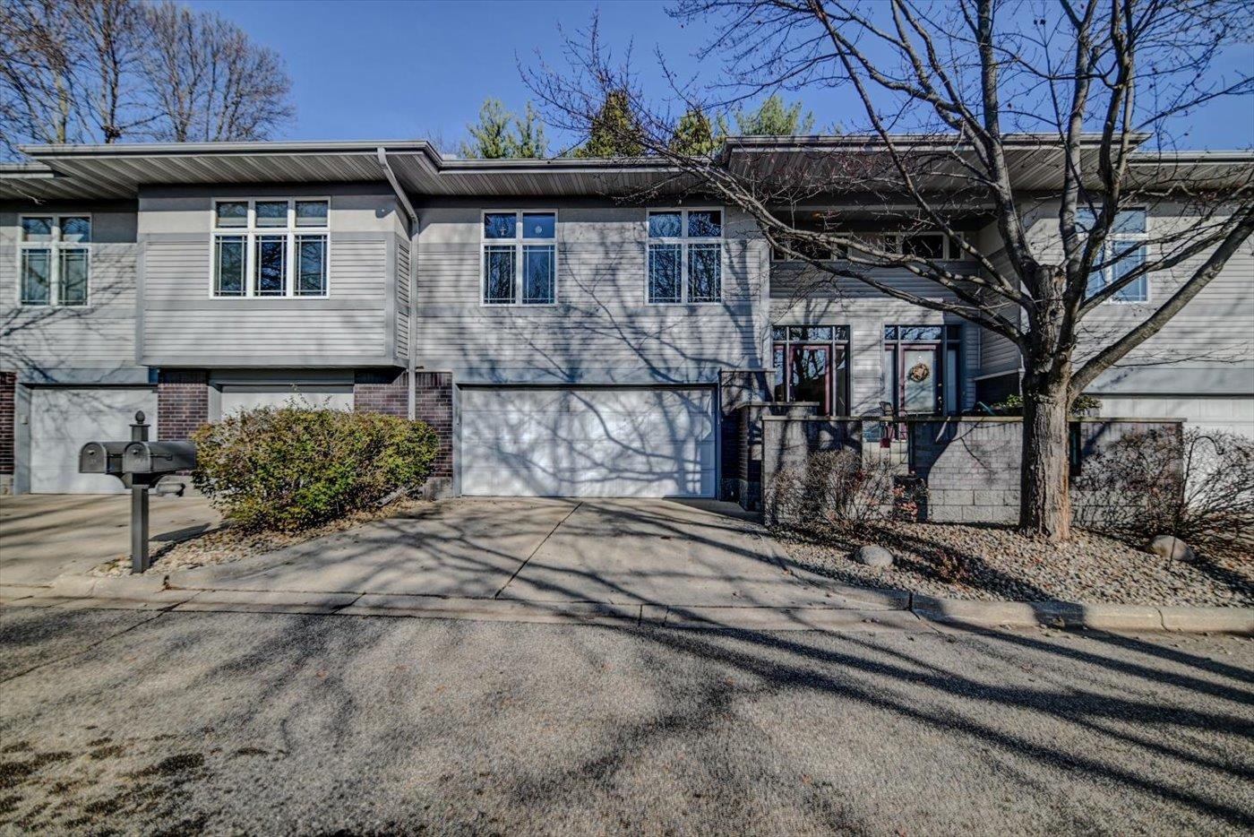 Two-story gray-sided attached home with an attached garage, wide driveway, and leafless tree.
