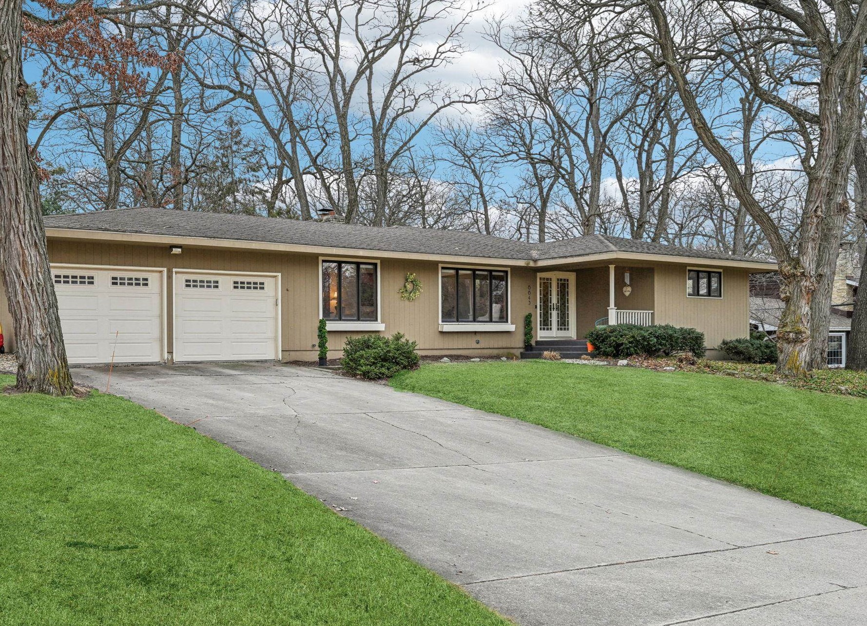 Tan single-story house with two garage doors, a covered entry, and a wide driveway.