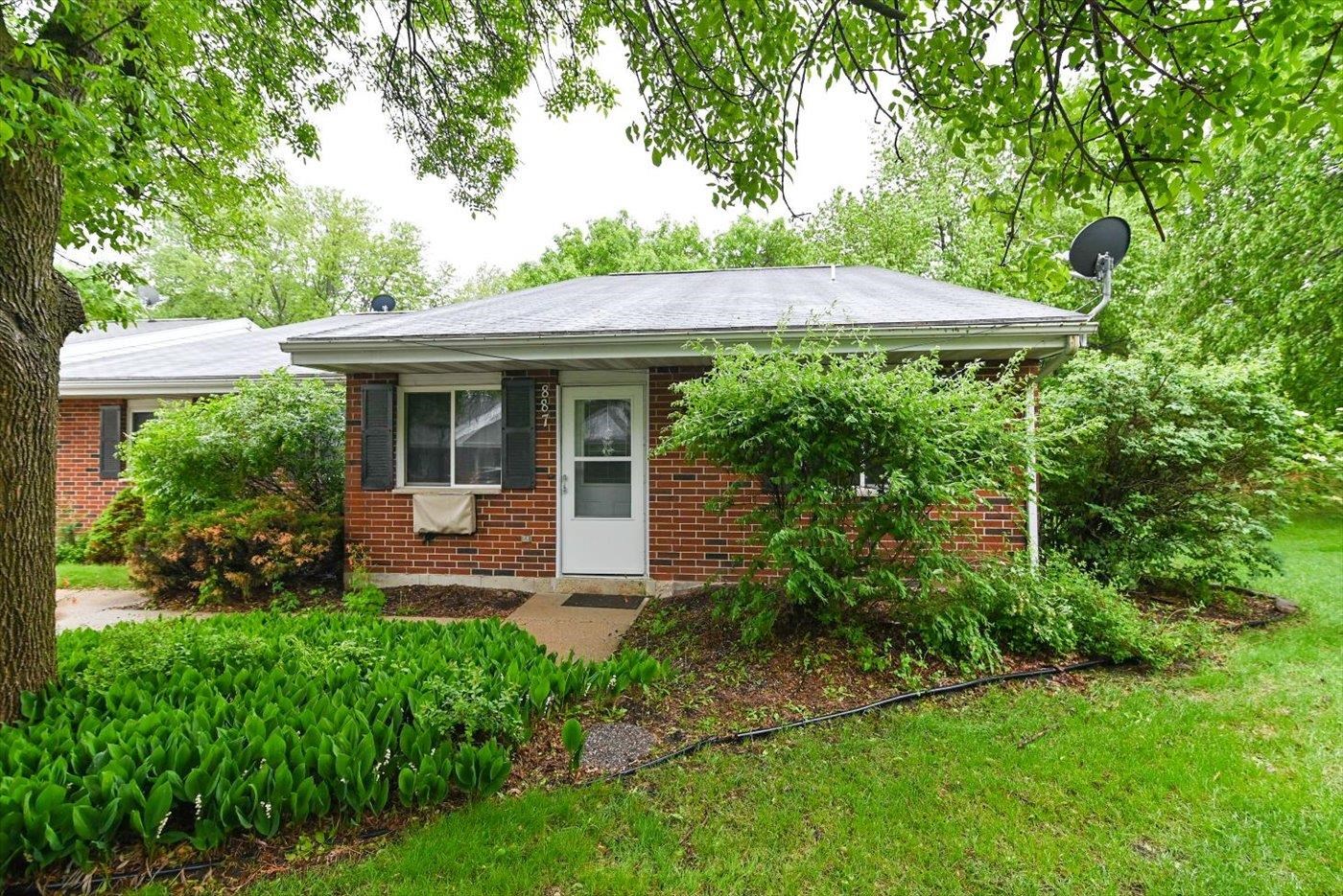 Red brick home with a white front door, framed by leafy trees and shrubs.