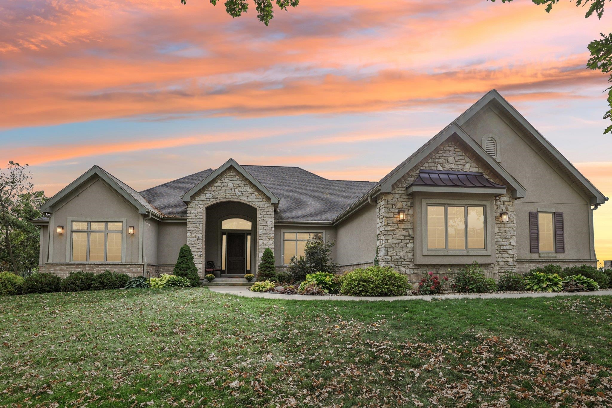 Stone-and-stucco home with landscaped lawn beneath a vivid sunset sky.