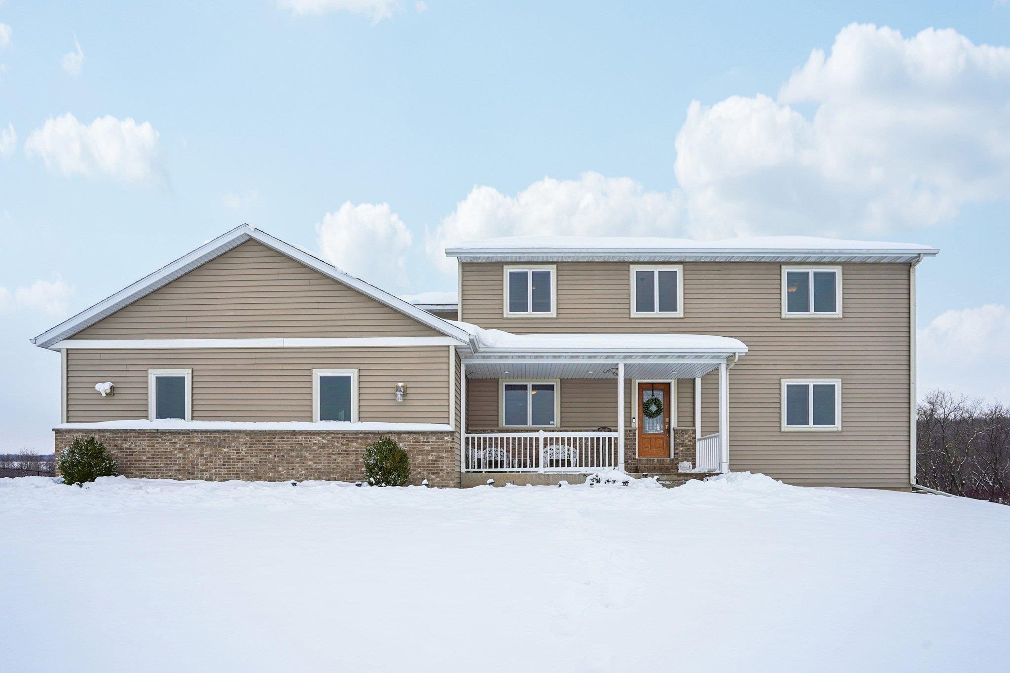 Two-story beige house with a covered porch and brick facade in a snow-covered yard.
