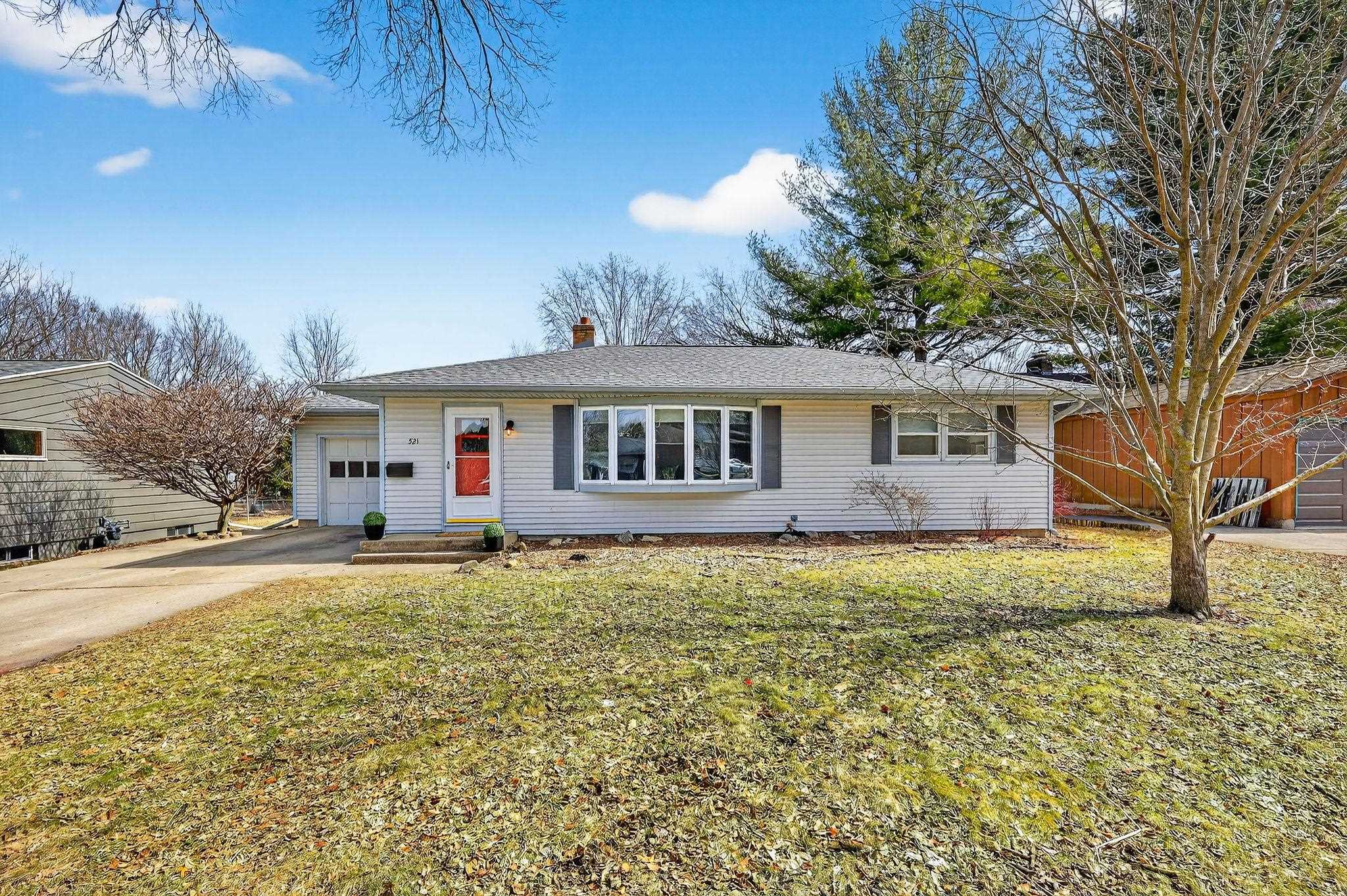Single-story house with a red front door, attached garage, and leafless trees in the yard.