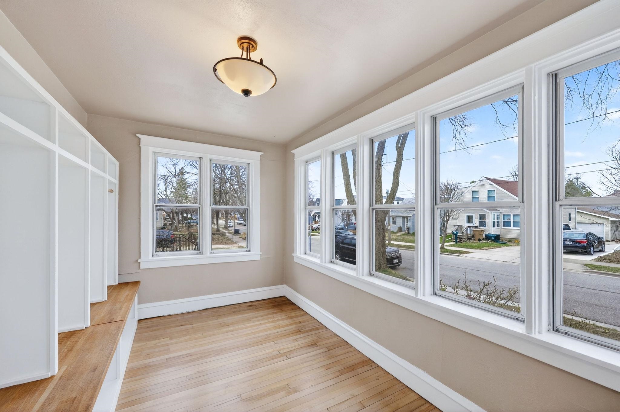 Bright sunroom with built-in white shelving, hardwood floors, and large street-facing windows.
