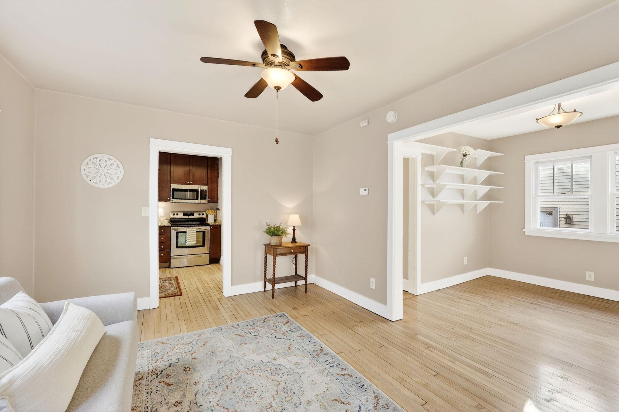 Living room with hardwood floors, ceiling fan, and open views into the kitchen and adjoining room.