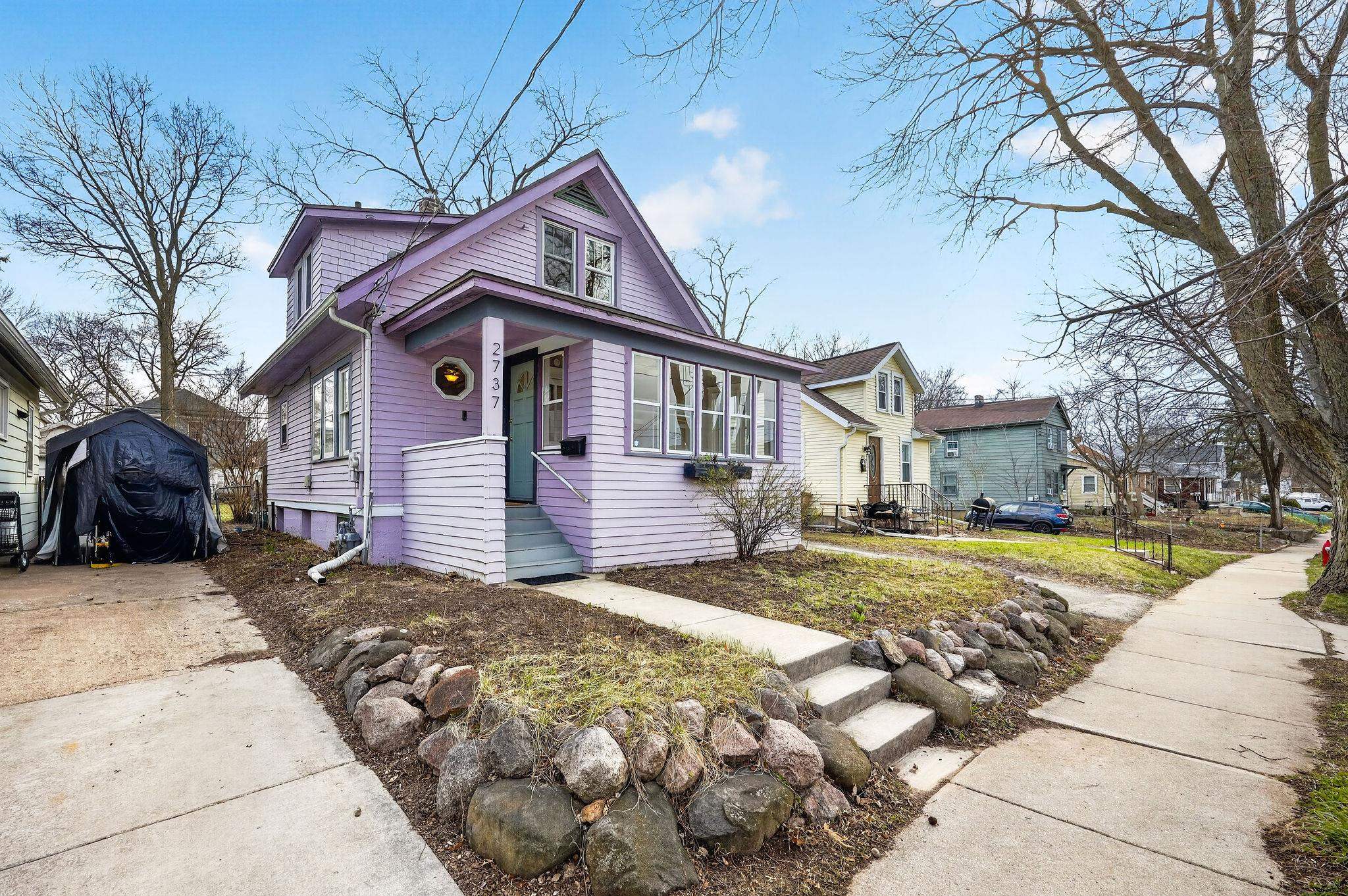 Lavender two-story house with a steep gabled roof, front walk, and stone-edged garden.