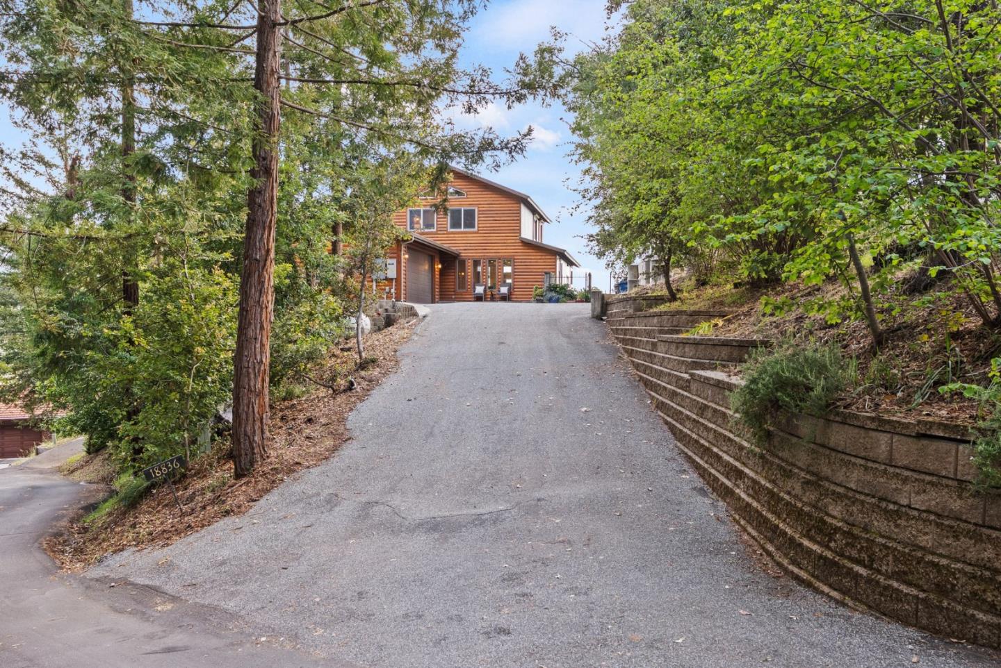 Wood-sided home at the top of a long driveway, surrounded by mature trees and a retaining wall.