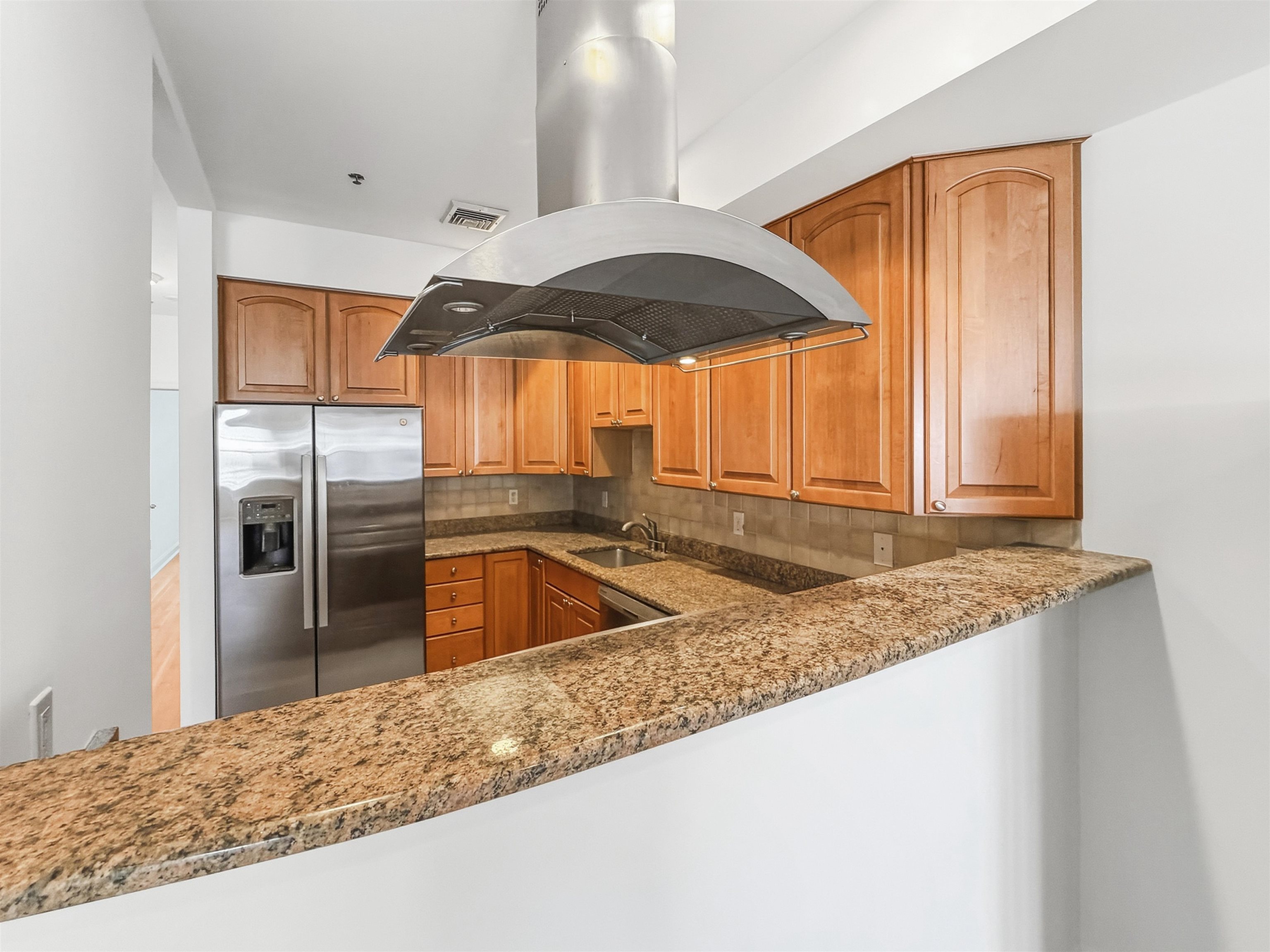 Kitchen with wood cabinets, granite breakfast bar, stainless refrigerator, and a large range hood.