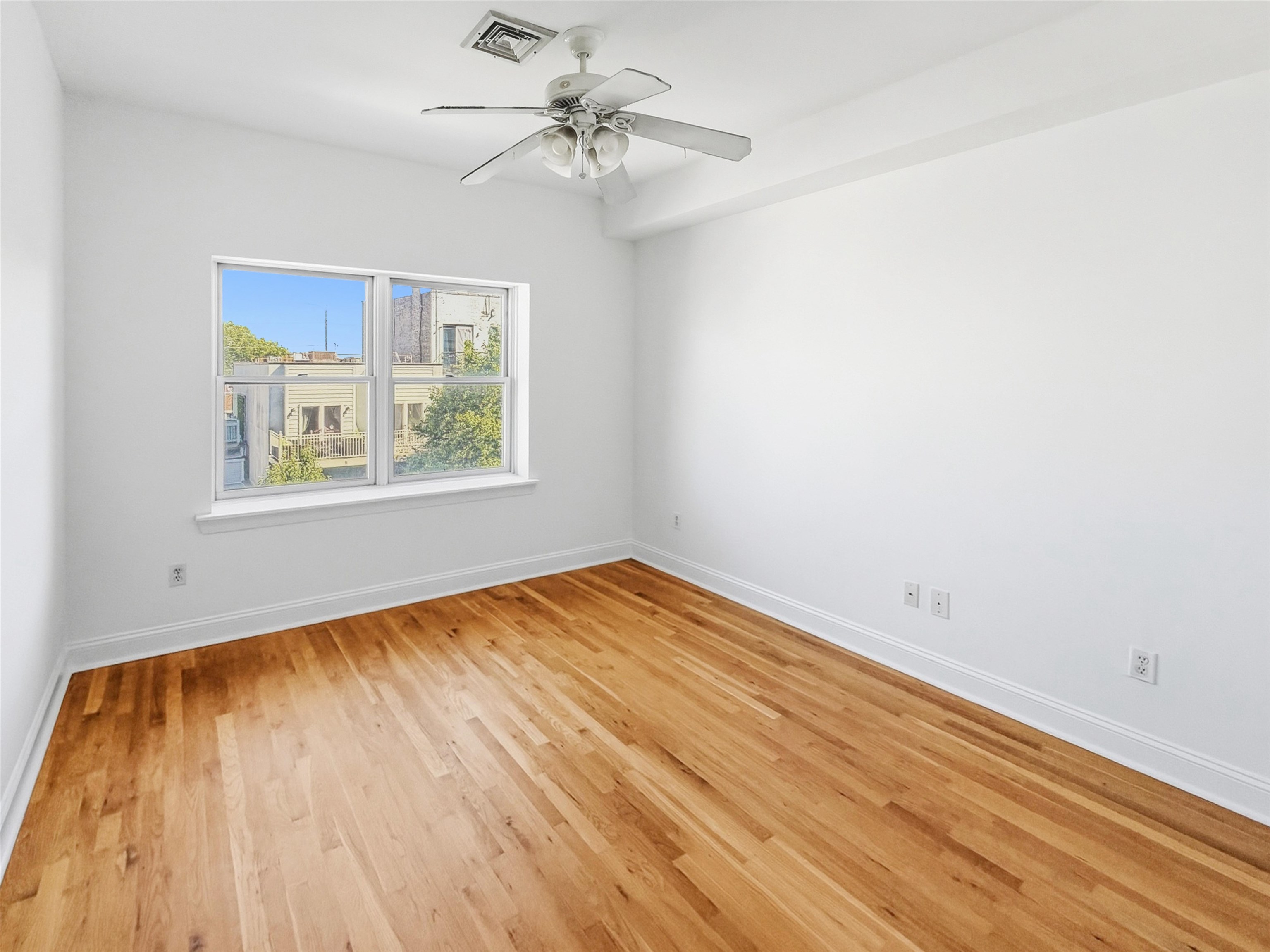 Empty room with hardwood floors, a ceiling fan, and a double window.
