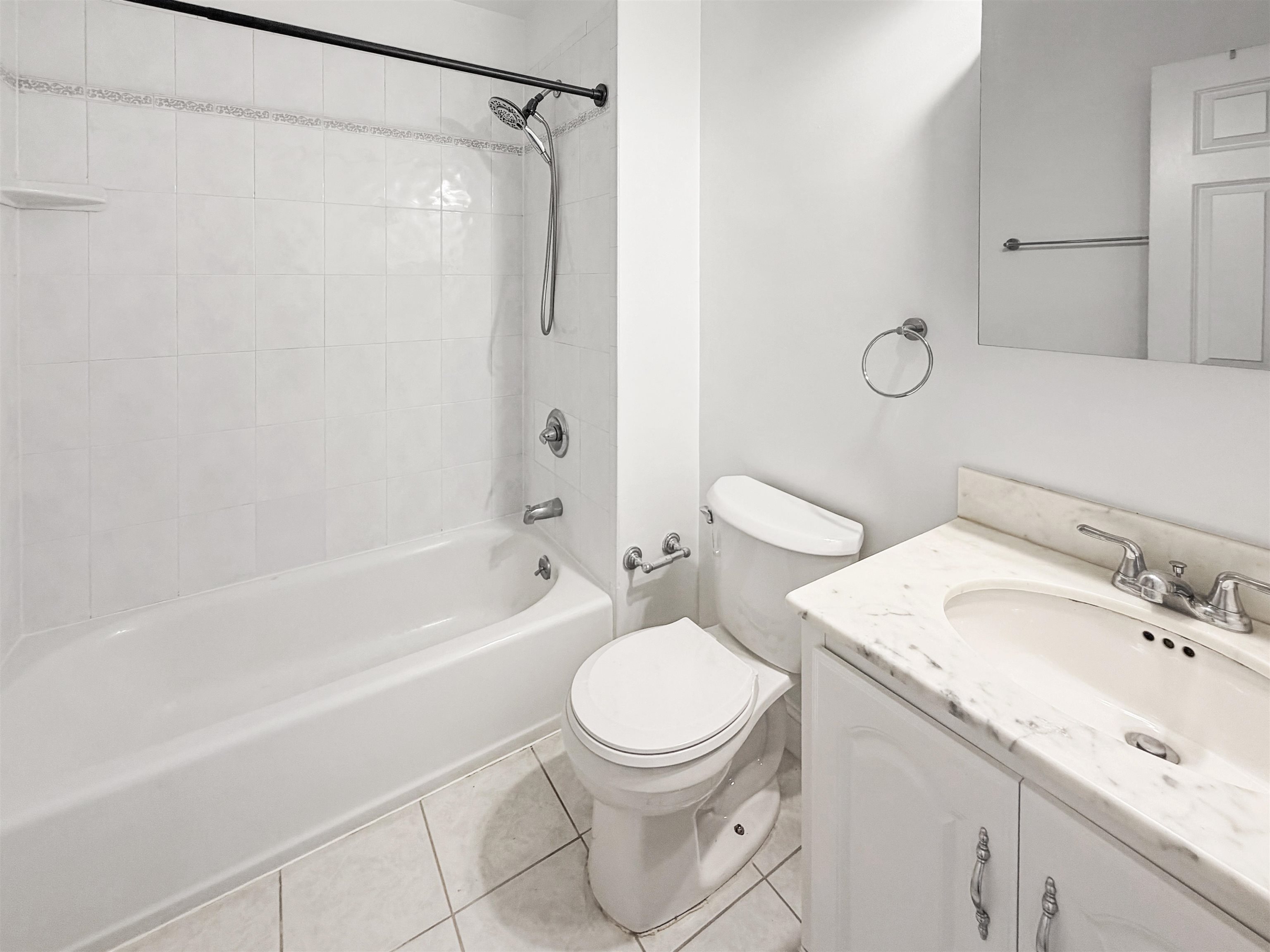 Bathroom with a tiled tub and shower, toilet, and marble-top vanity.