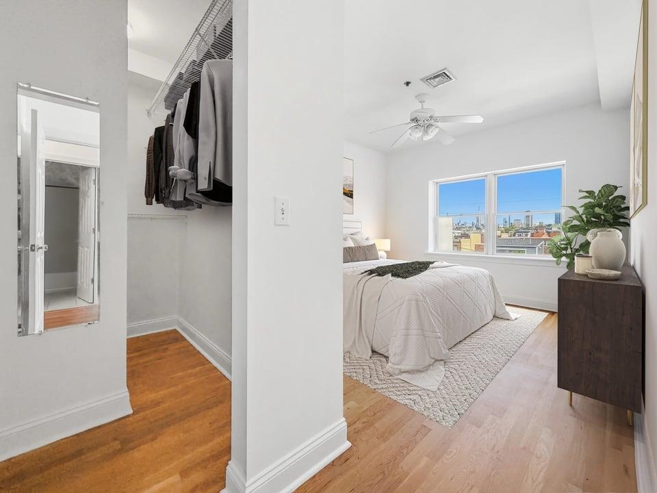 Furnished bedroom with a walk-in closet and city buildings visible through the window.