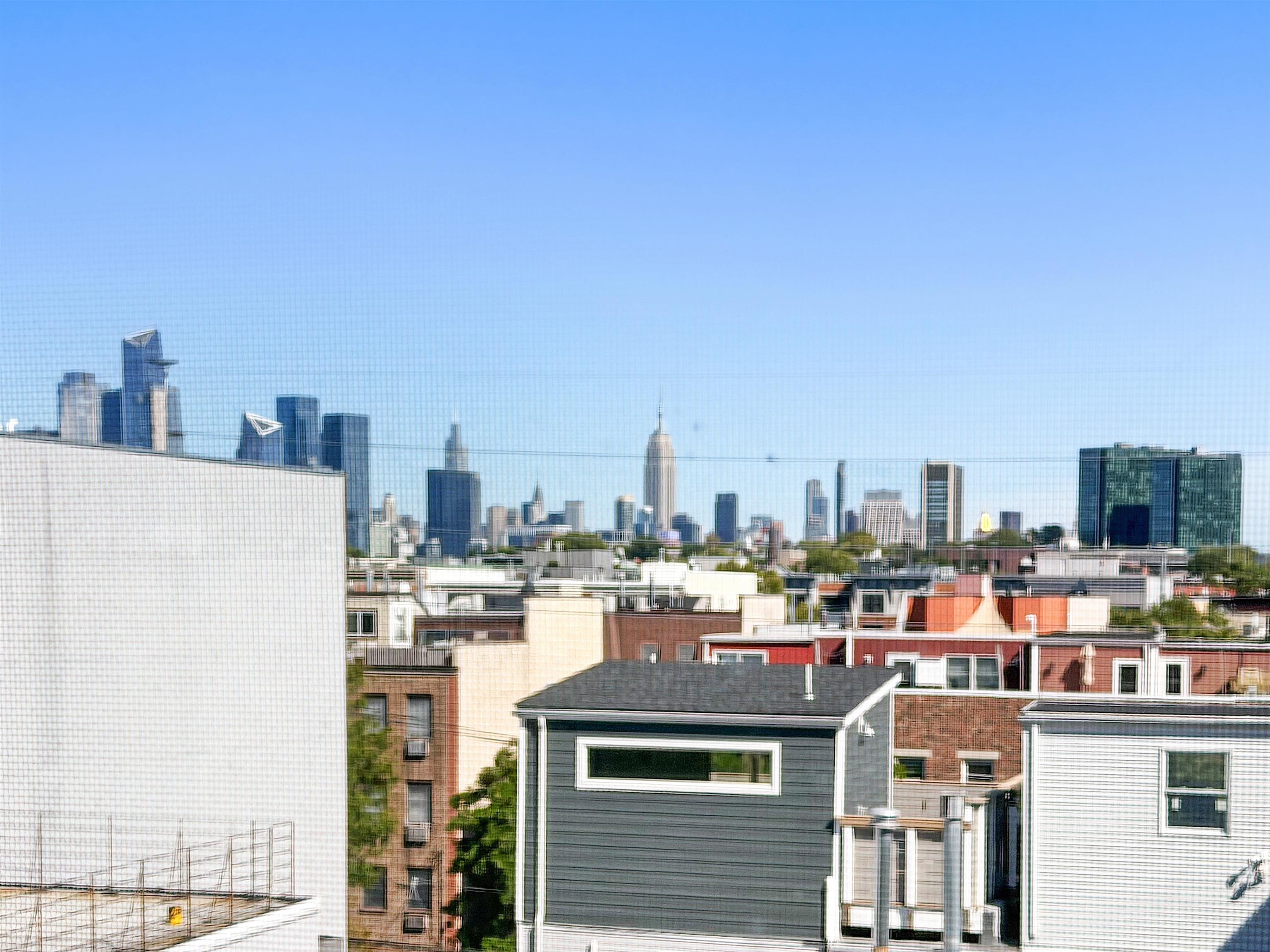 Manhattan skyline beyond Hoboken rooftops, seen through a fine safety mesh.