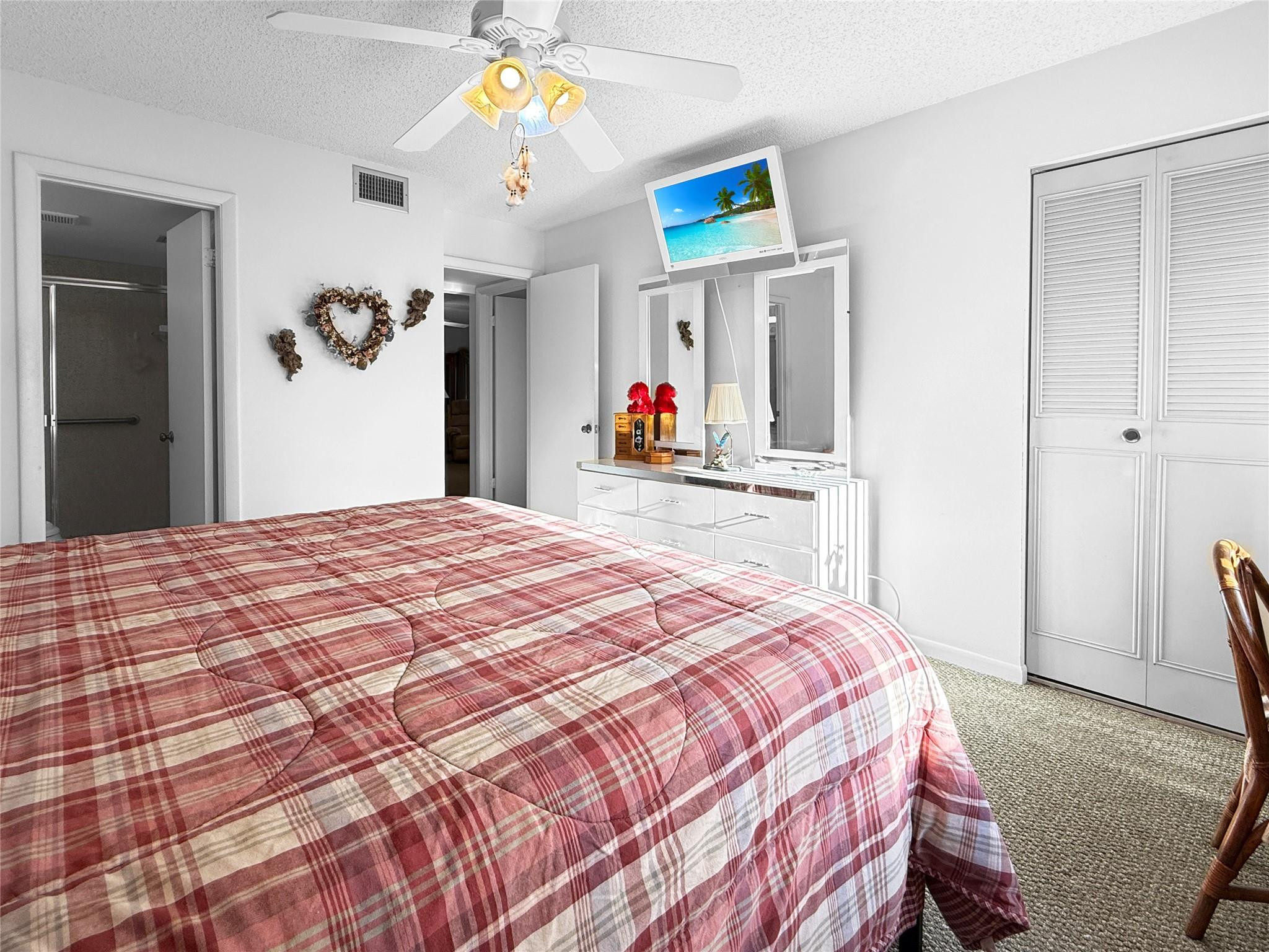 Bedroom with a red plaid bedspread, mirrored dresser, ceiling fan, and louvered closet doors.