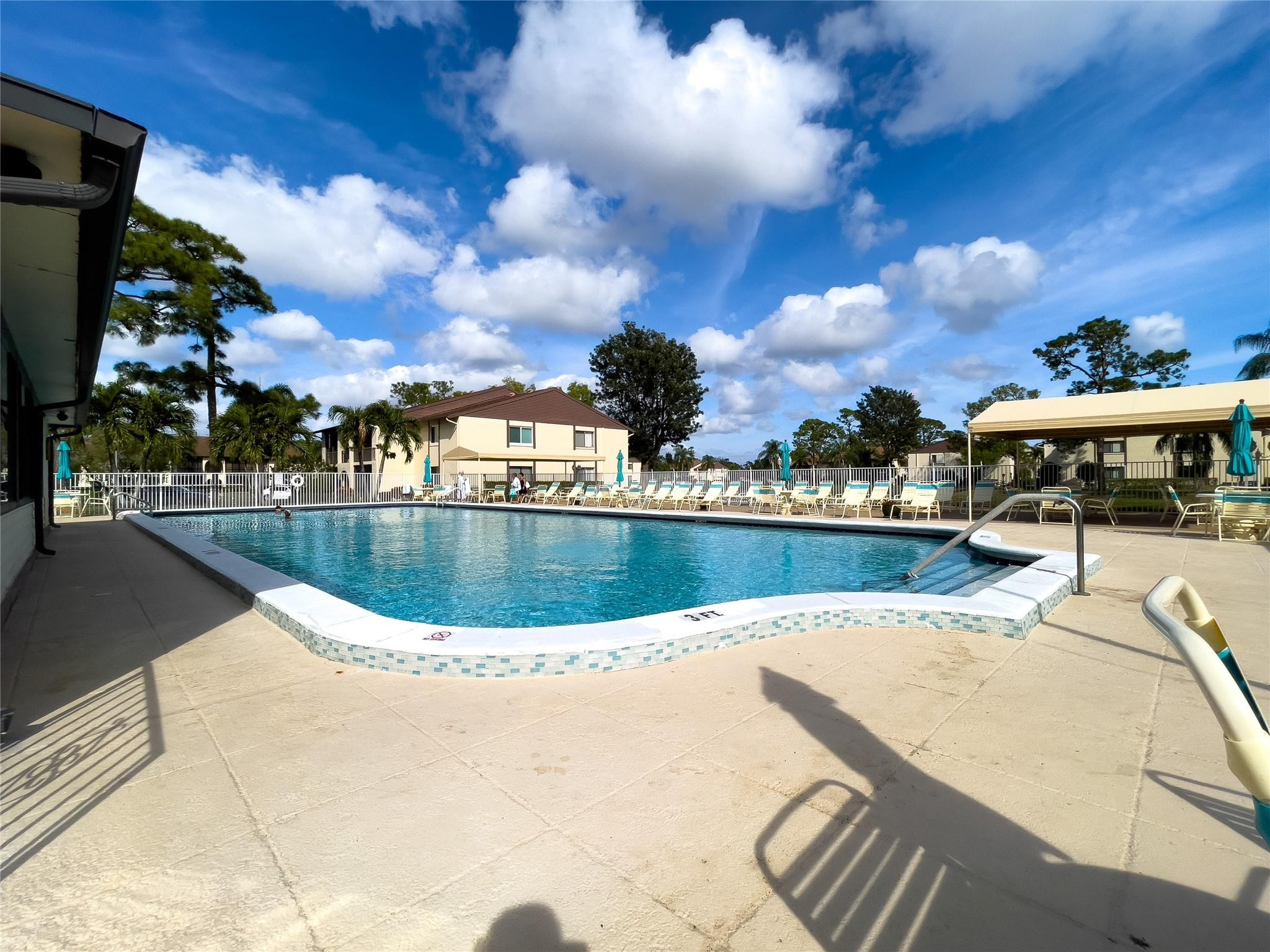 Community swimming pool with lounge chairs, a shade canopy, and palm trees.