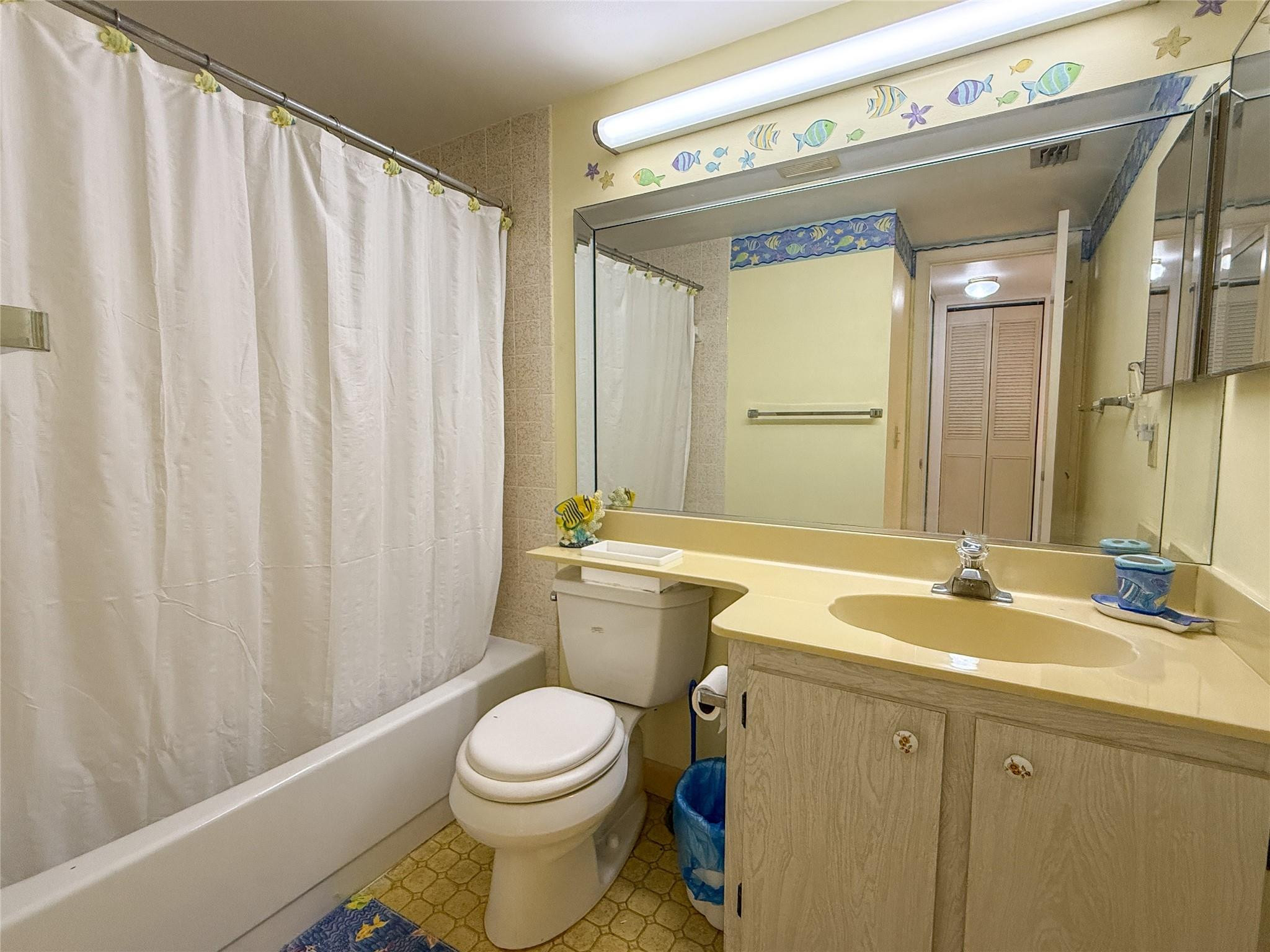 Bathroom with a white shower curtain, yellow vanity, large mirror, and colorful fish decorations.