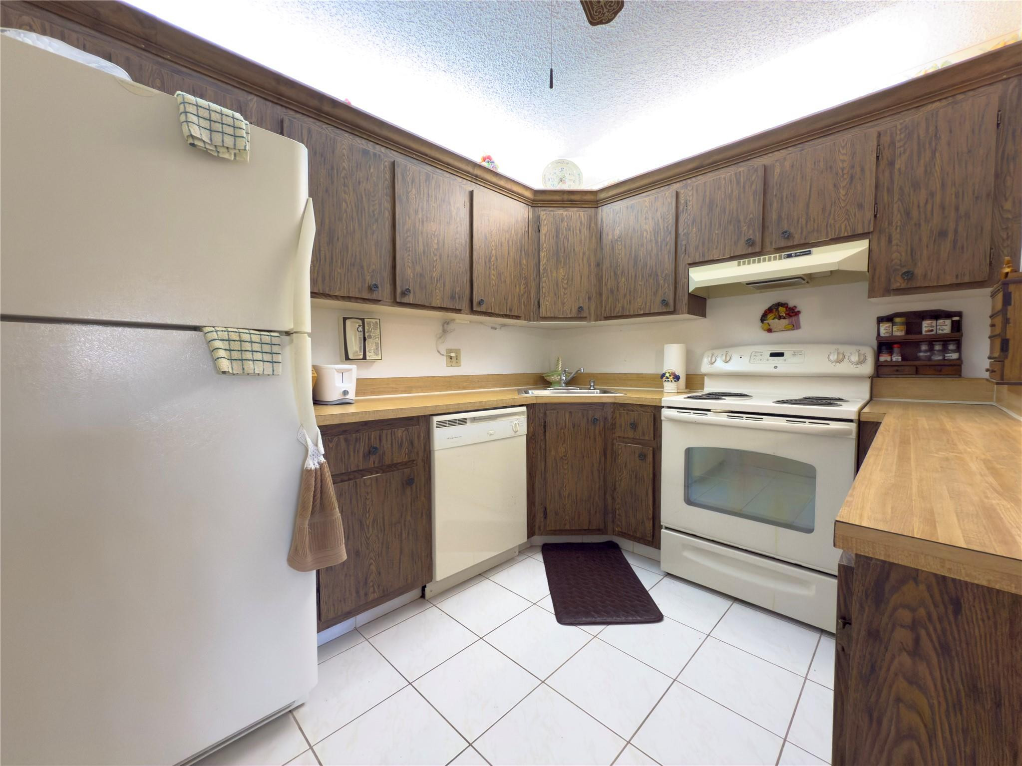 Kitchen with dark wood cabinets, white appliances, and tiled floor.