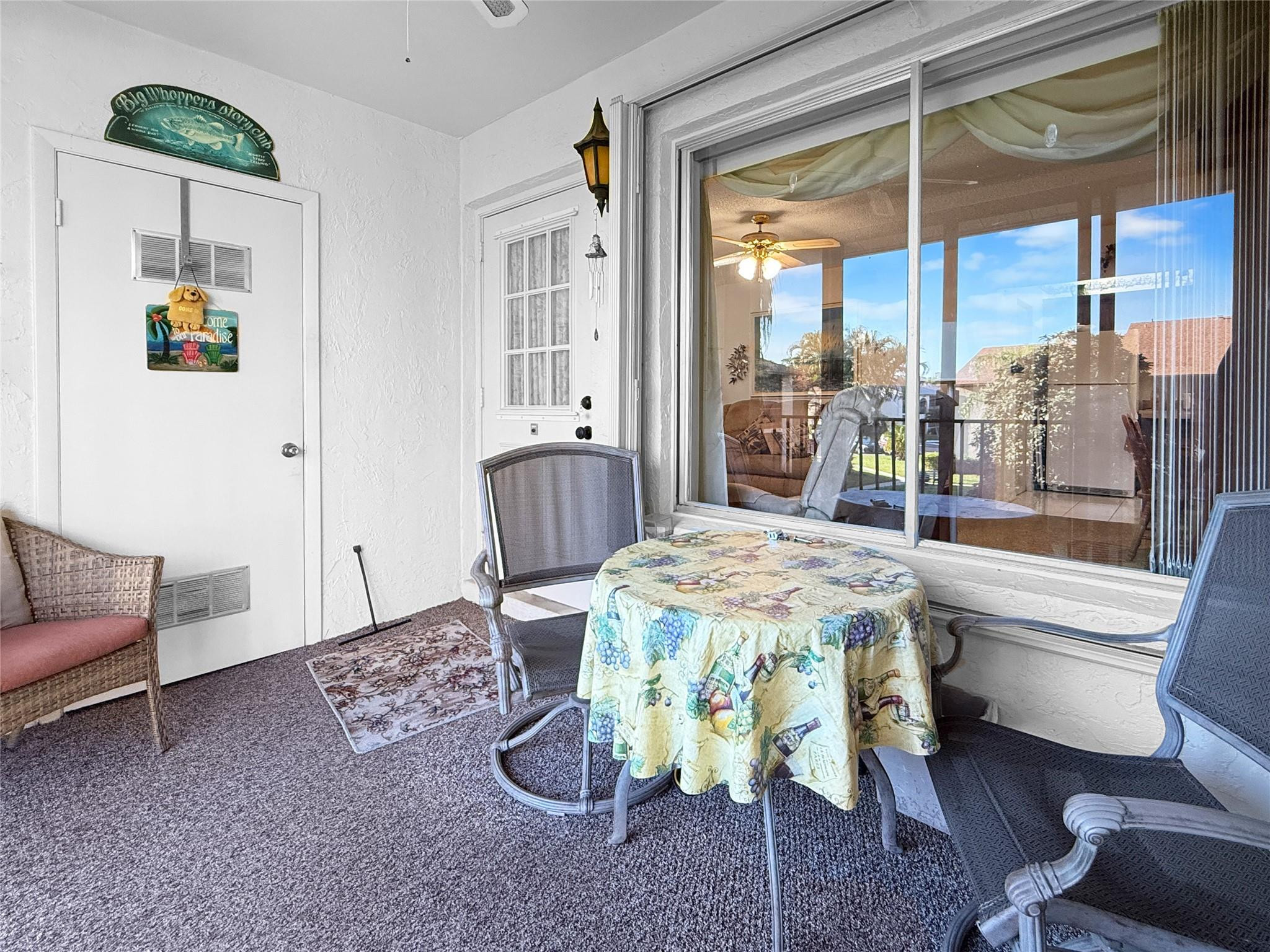 Enclosed patio with a round patterned table, wicker chairs, and a large window overlooking the courtyard.