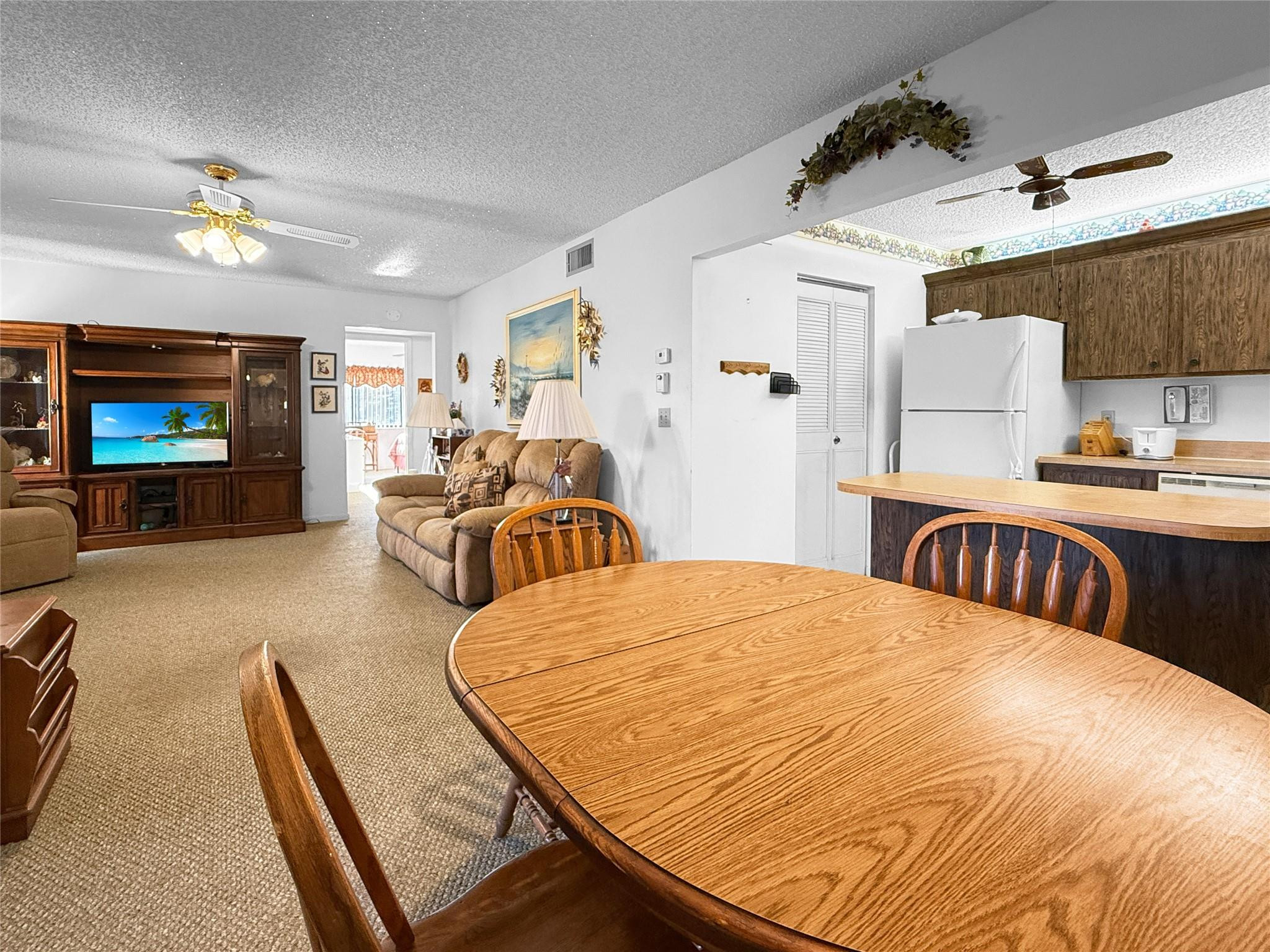 Open-plan living and dining area with a large wooden table, tan sofa, and kitchen peninsula.