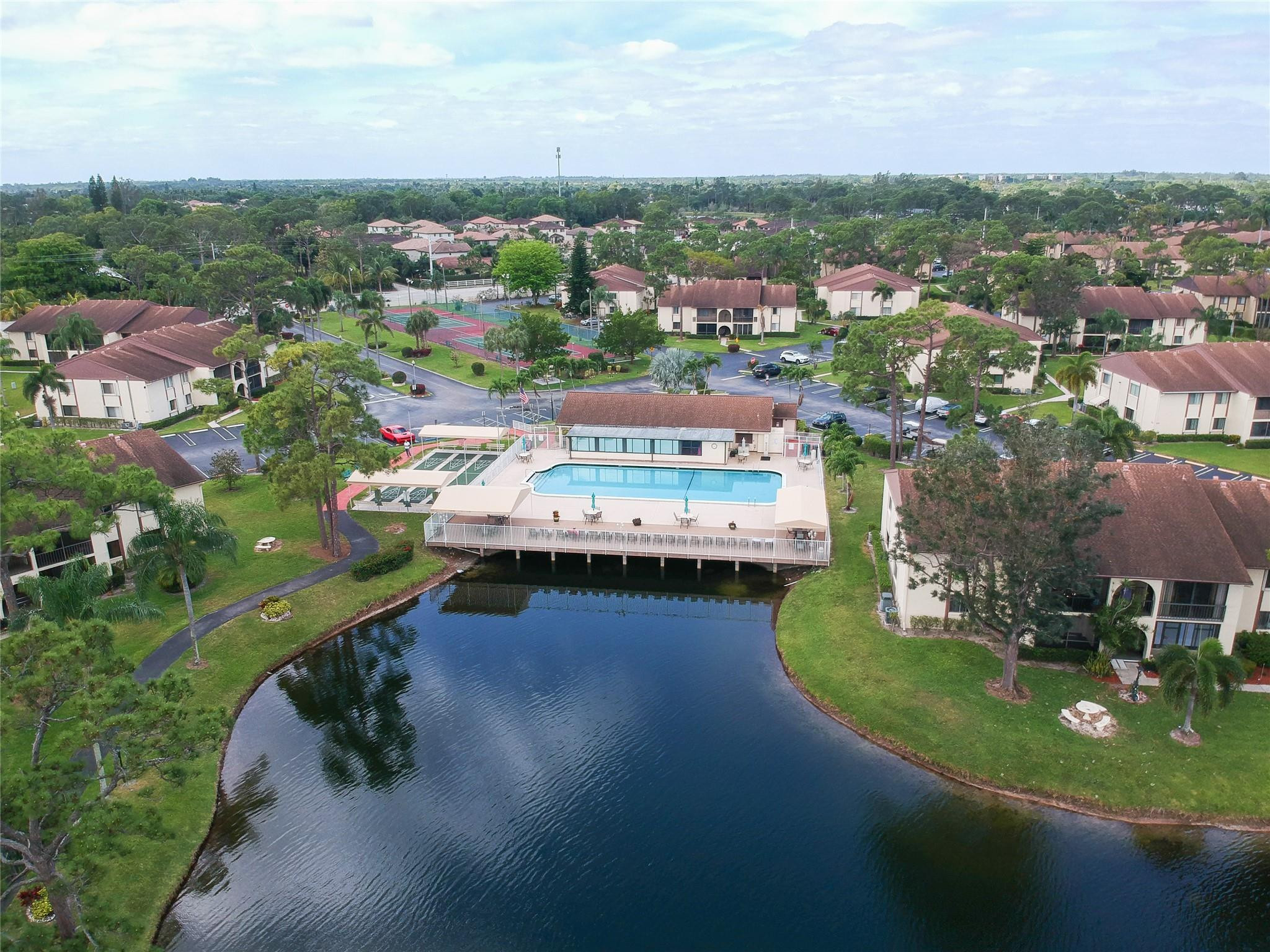 Condominium community with a pool and tennis courts beside a landscaped lake.