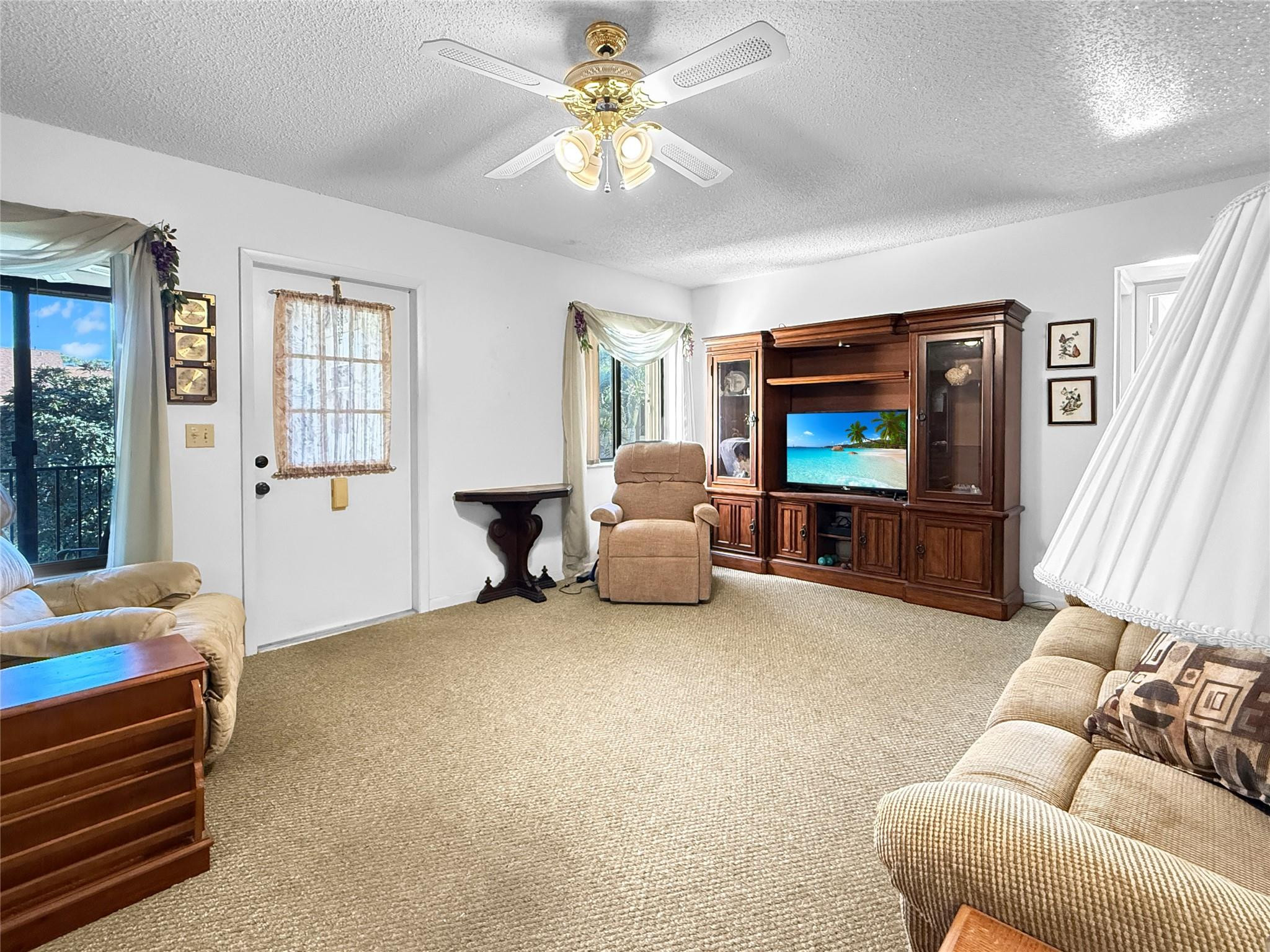 Furnished living room with beige sofas, carpet, and a dark wood entertainment center.