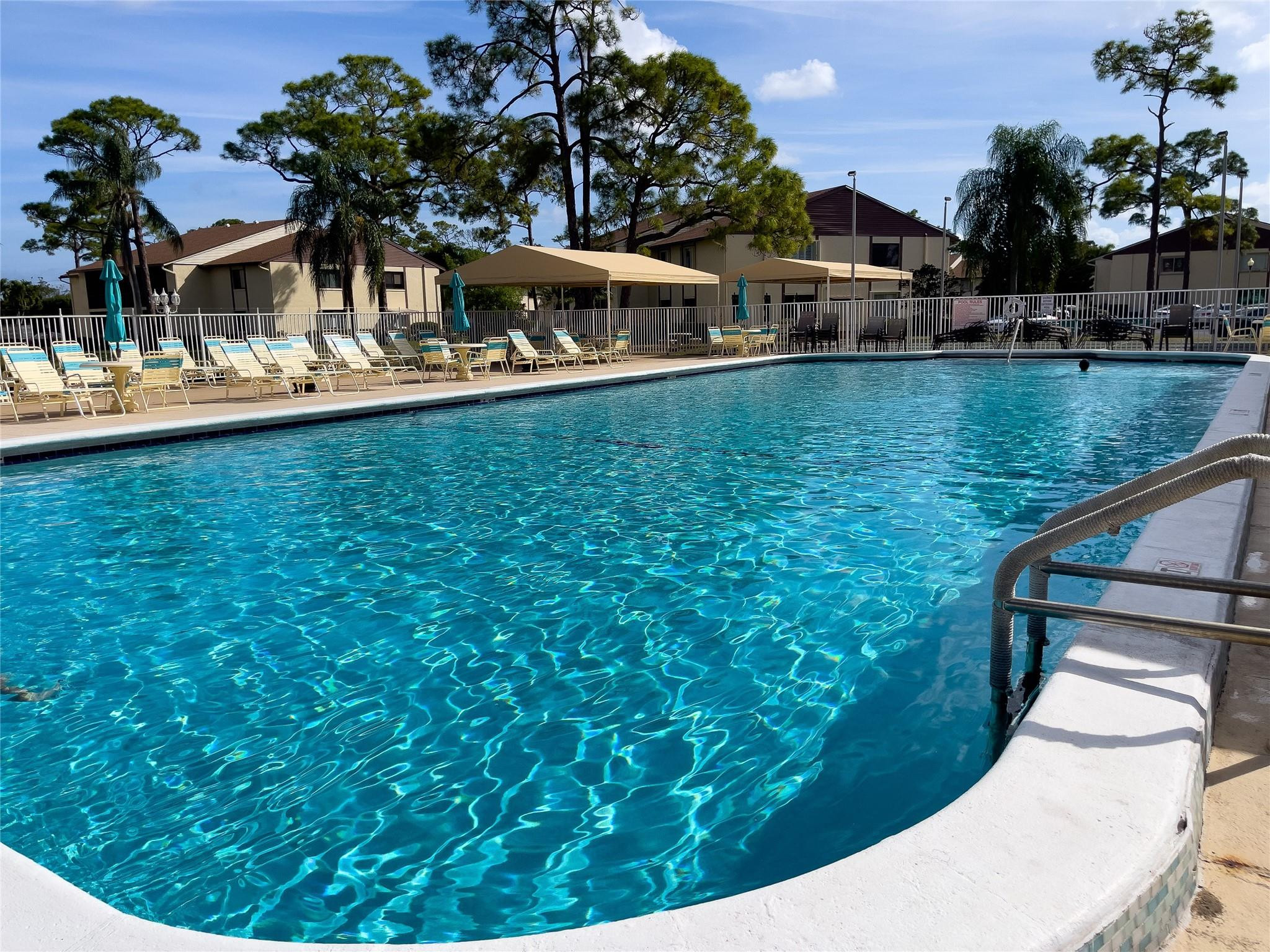 Community swimming pool with lounge chairs and shade canopies beside apartment buildings.