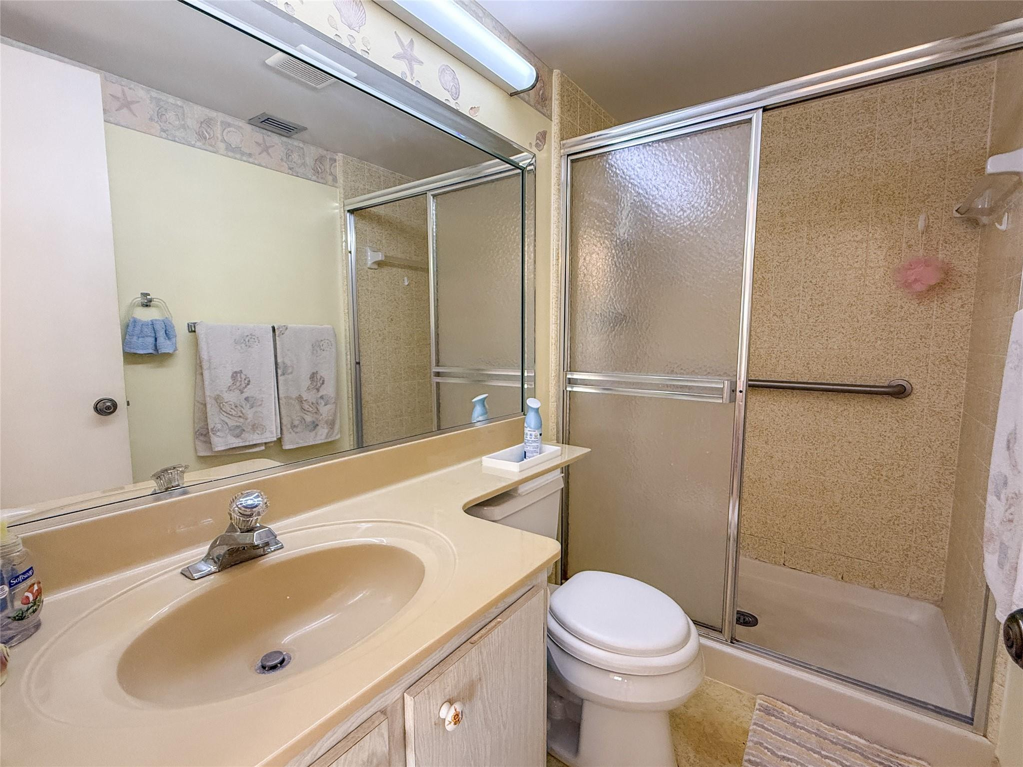 Bathroom with a beige vanity, large mirror, toilet, and tiled shower with sliding doors.