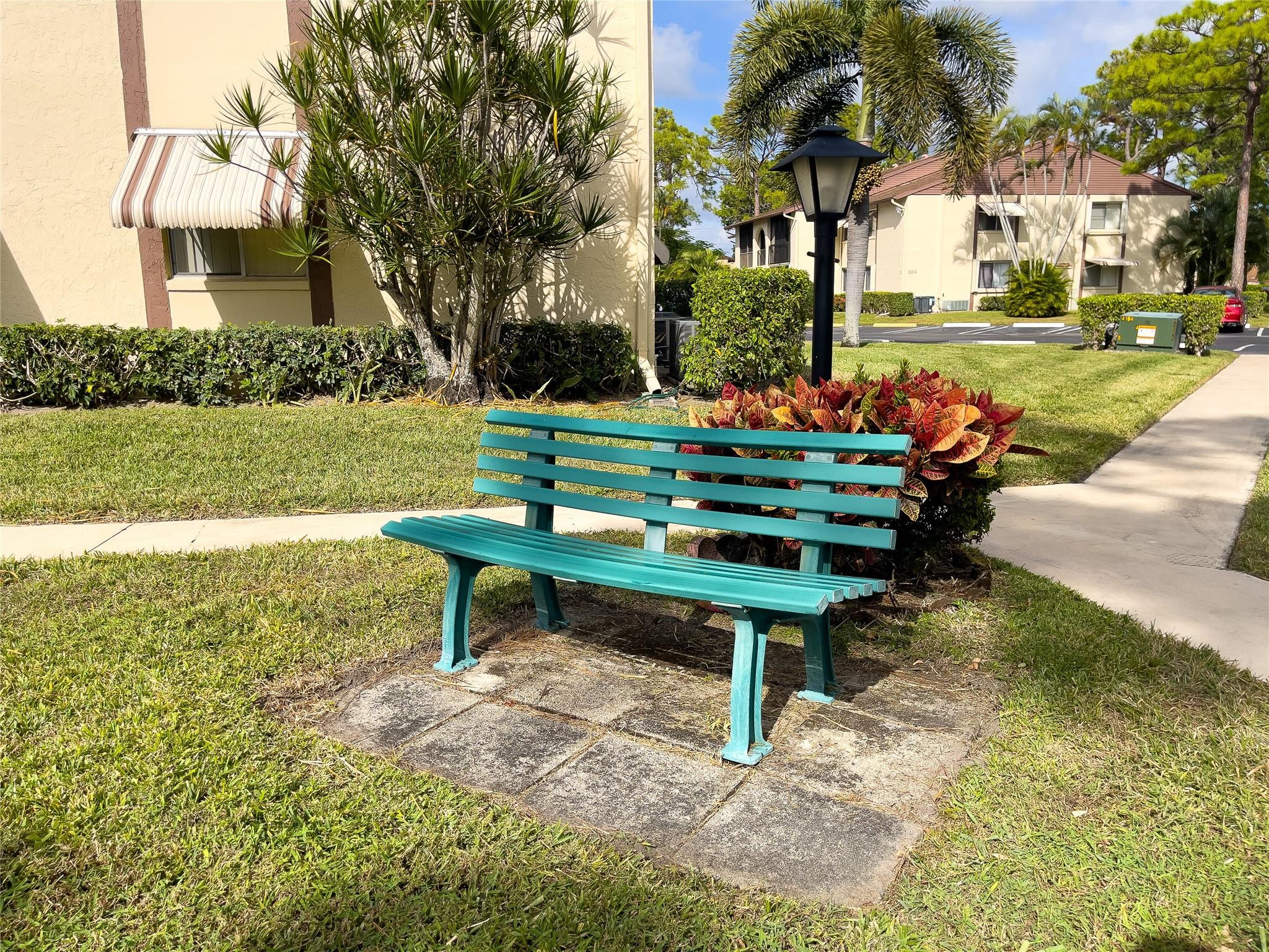 Turquoise bench in landscaped condominium grounds, with palm trees and tan buildings behind it.